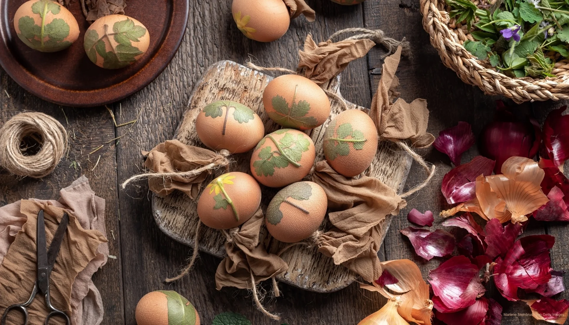 Ostereier mit Blättern und Kräutern dekoriert auf Holzbrett und Zwiebelhäuten