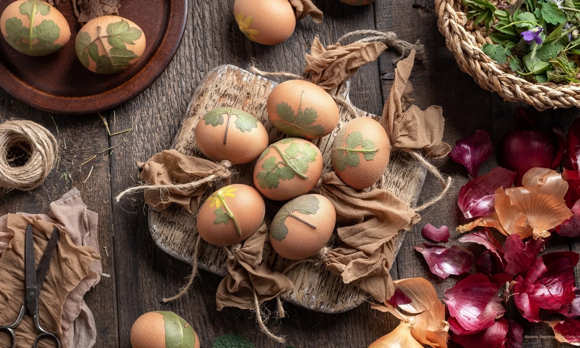 Ostereier mit Blättern und Kräutern dekoriert auf Holzbrett und Zwiebelhäuten