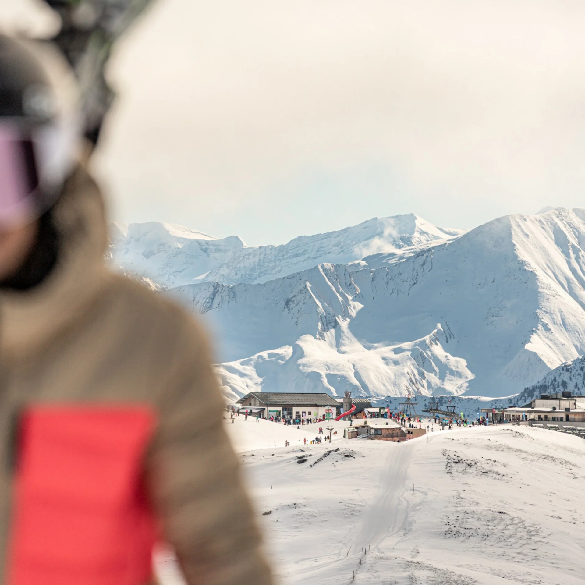 Ski.Delight Snowy mountain station and ski lifts beneath high peaks, with a blurred person in the foreground