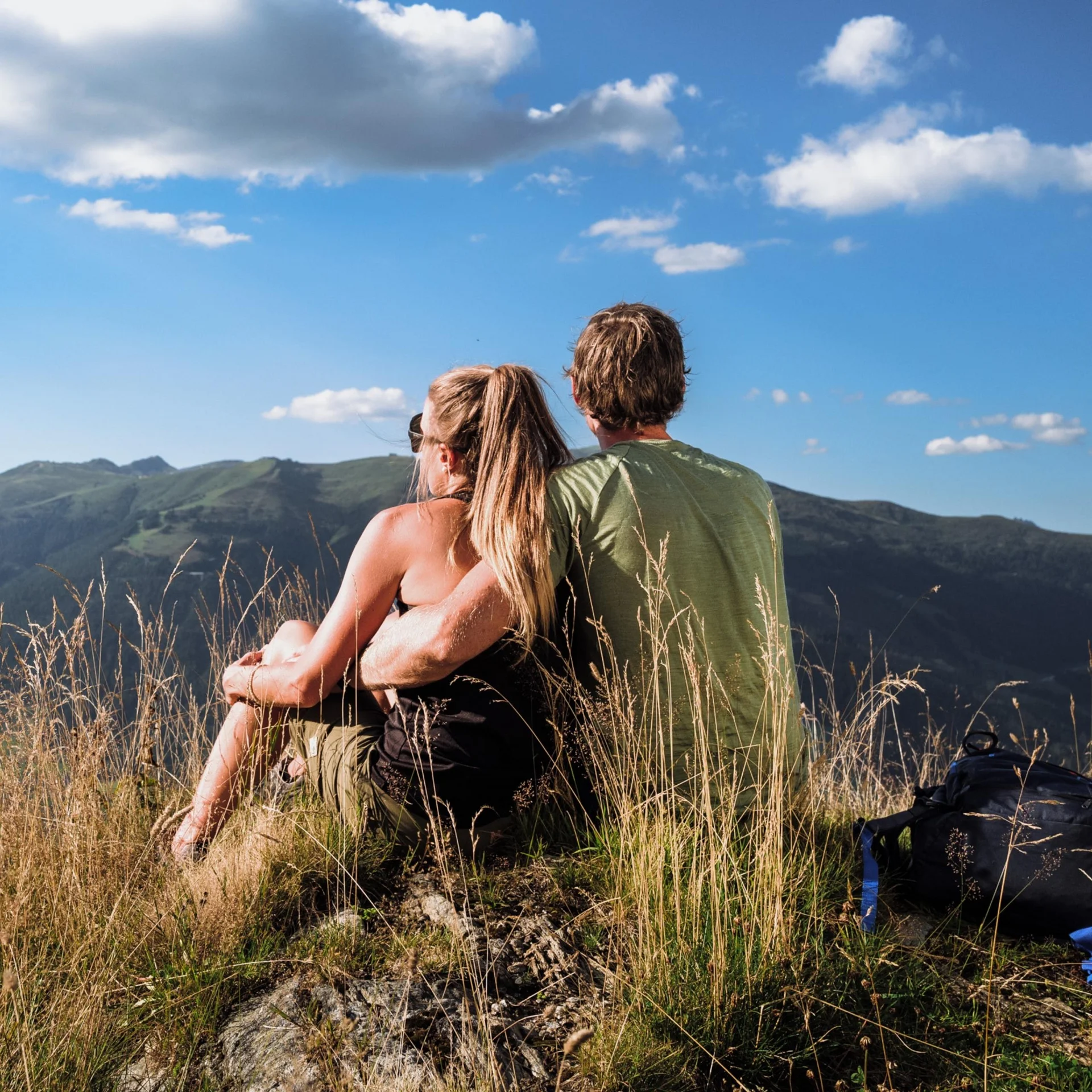 Couple sitting on hill overlooking mountains under blue sky