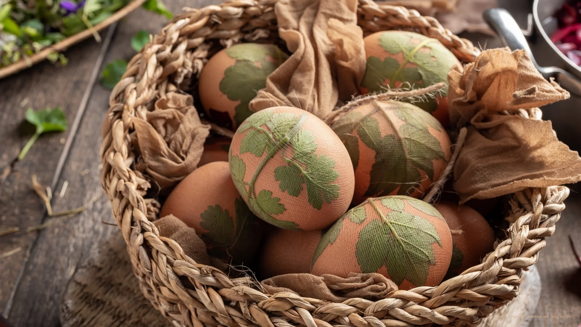 Ostereier mit grünen Blattmustern in einem Korb auf Holztisch