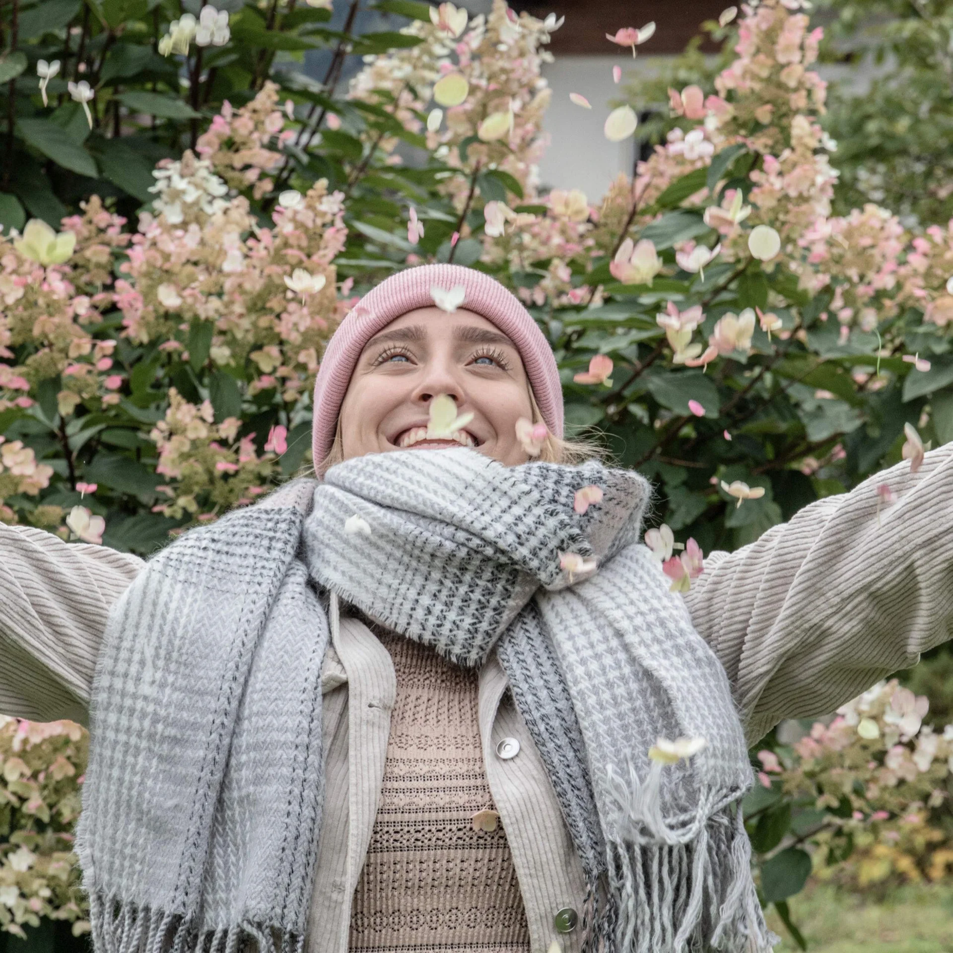 Herbstkinder unter sich Frau mit pinker Mütze und Schal wirft Herbstblätter in die Luft