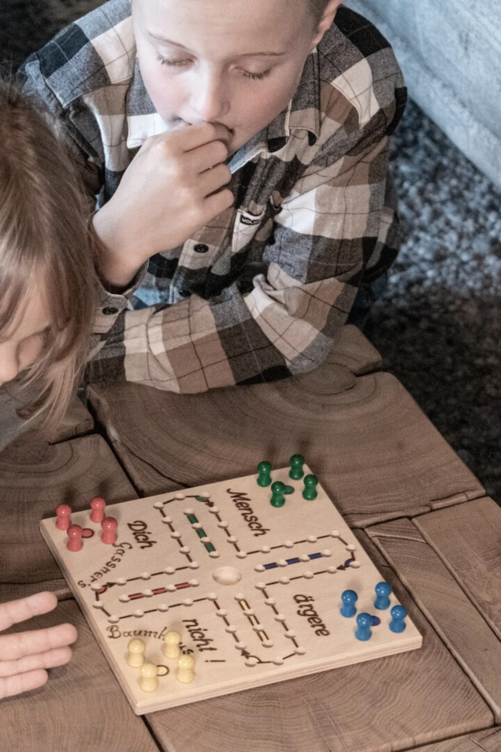 Vier Kinder spielen Mensch-ärgere-dich-nicht auf einem Holztisch