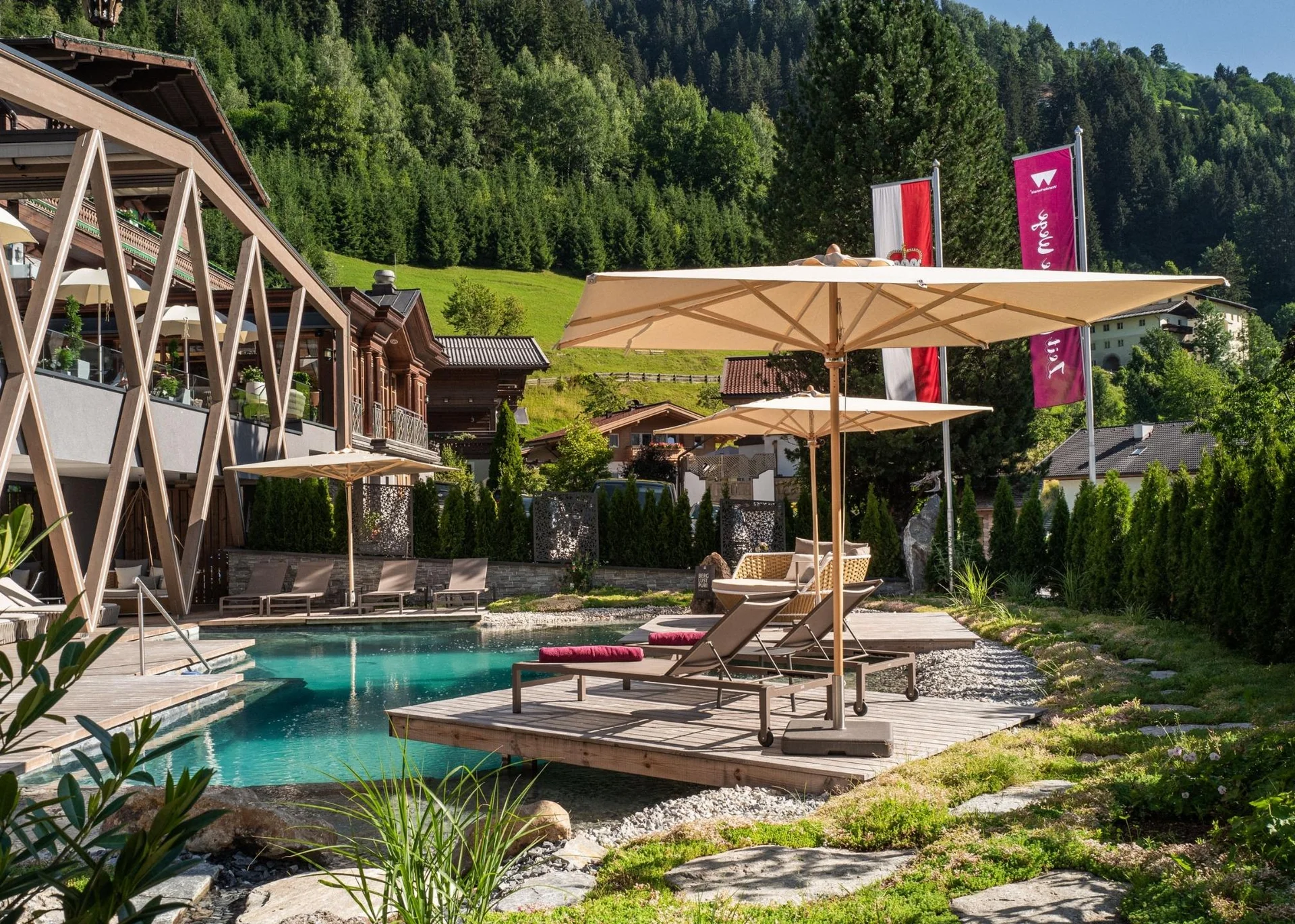 Entspannungsbereich mit Pool, Liegestühlen und Sonnenschirmen vor bewaldetem Hügel