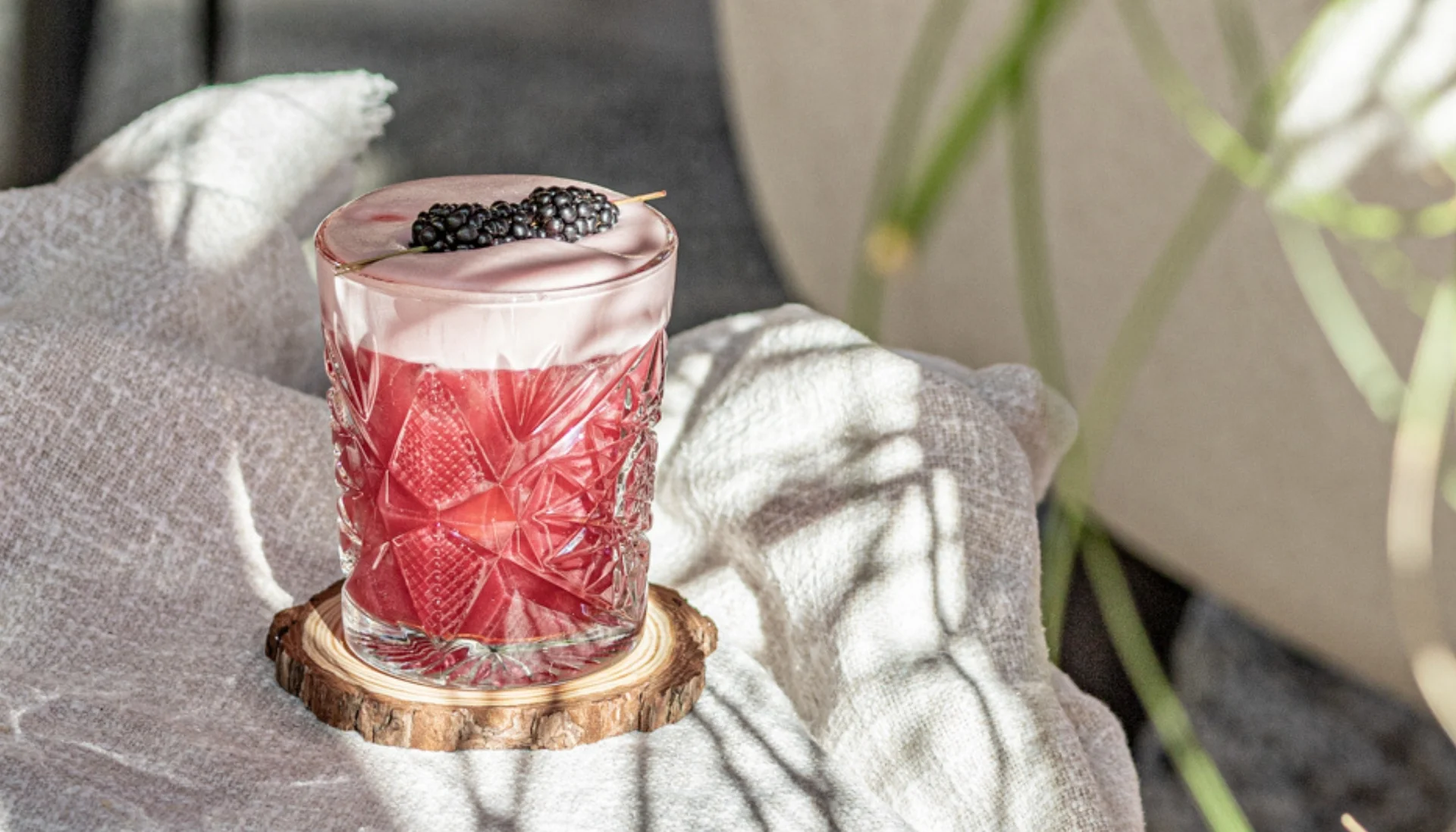 Rotes Getränk mit Schaum und Brombeeren in einem verzierten Glas auf Holzuntersetzer