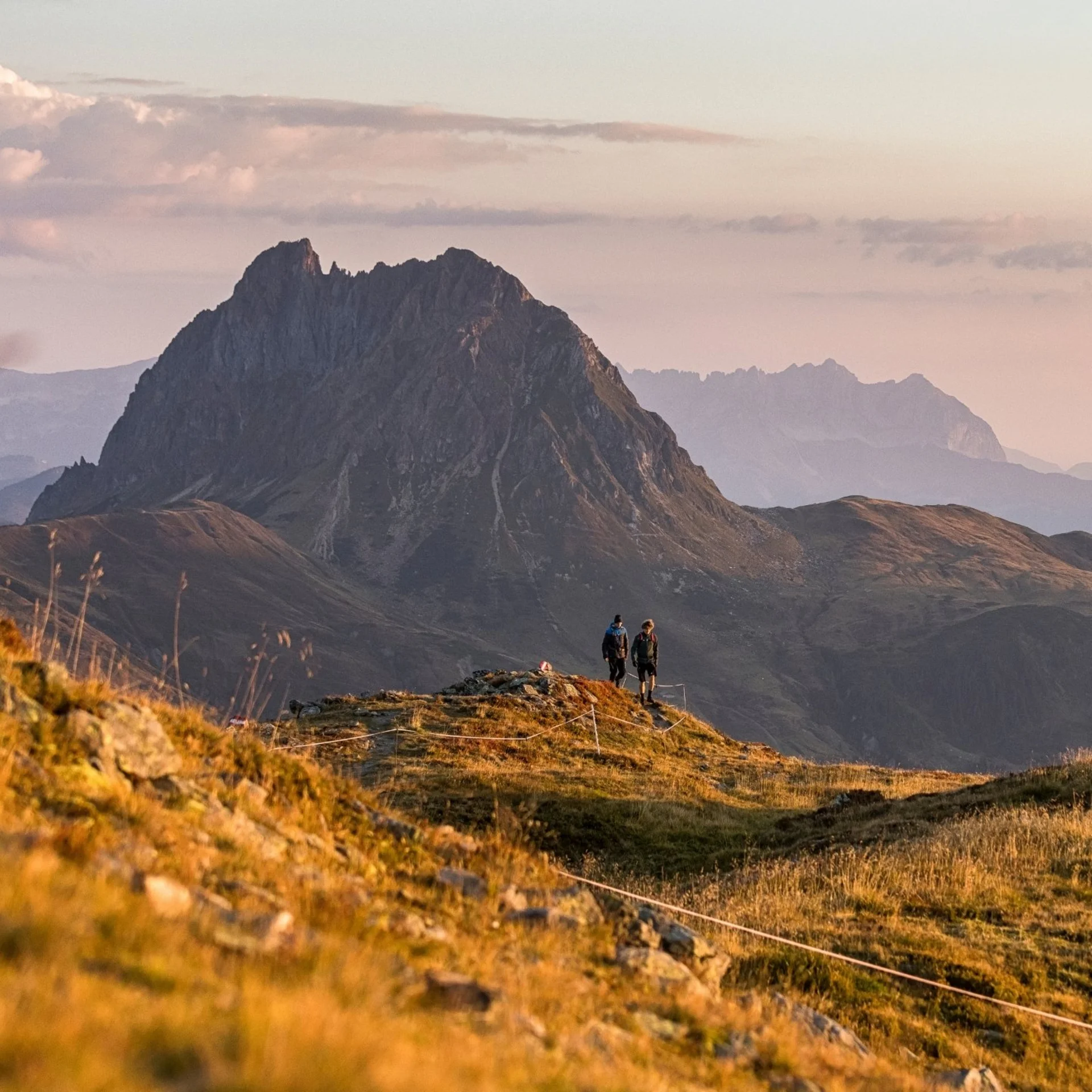 Wanderer auf einem Pfad mit Blick auf einen markanten Berg bei Sonnenuntergang
