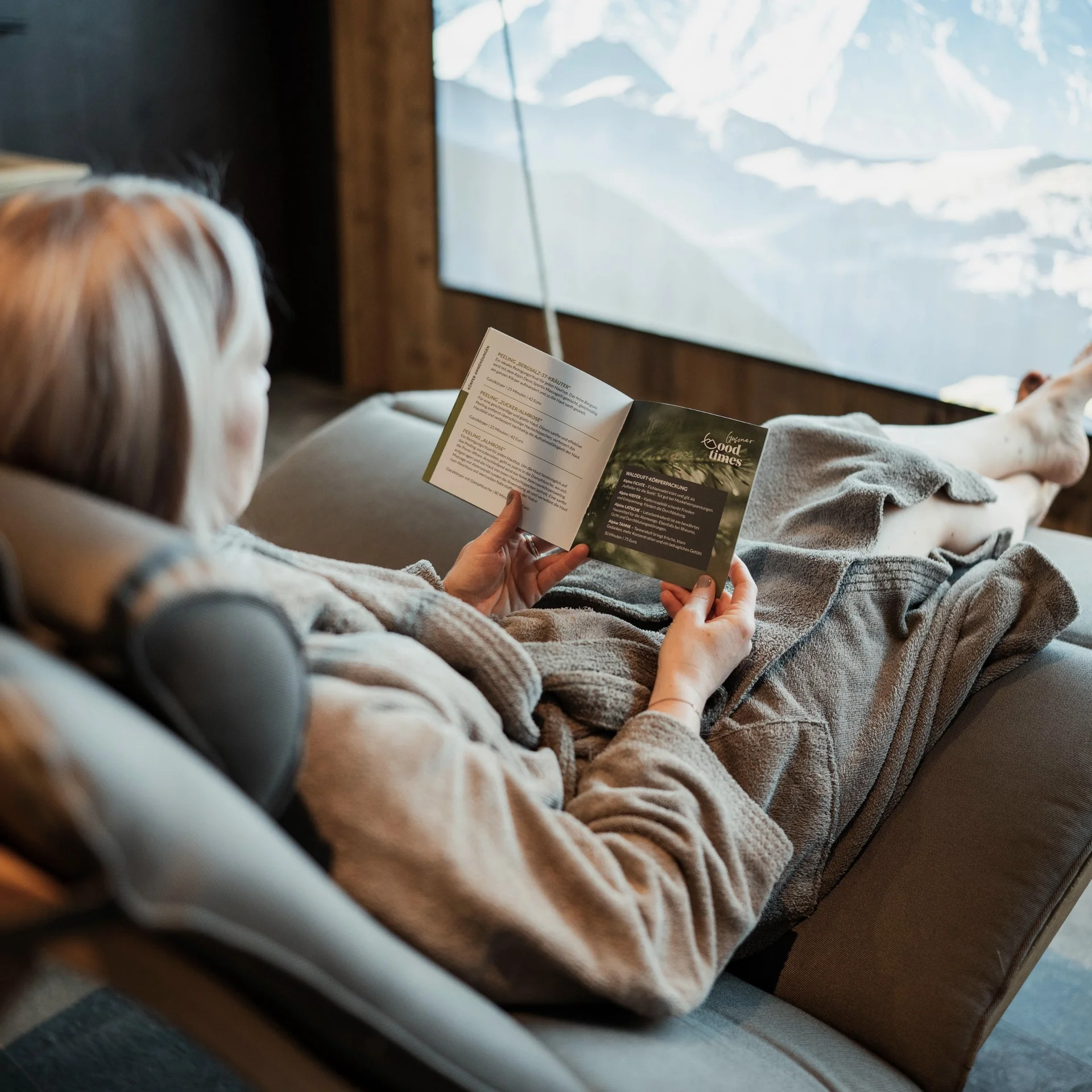 Home Person entspannt auf Sofa mit Broschüre, Blick auf Bergpanorama im Hintergrund