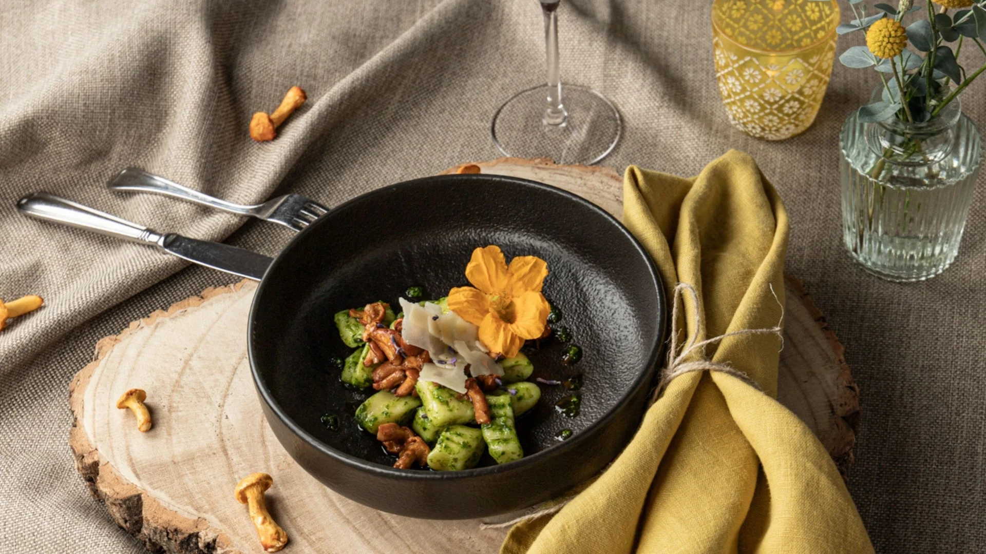 Gregors Sommerrezept: Gnocchi mit Basilikumpesto und Eierschwammerln Schwarze Schale mit Gnocchi, Pilzen und essbarer Blume auf Holzbrett