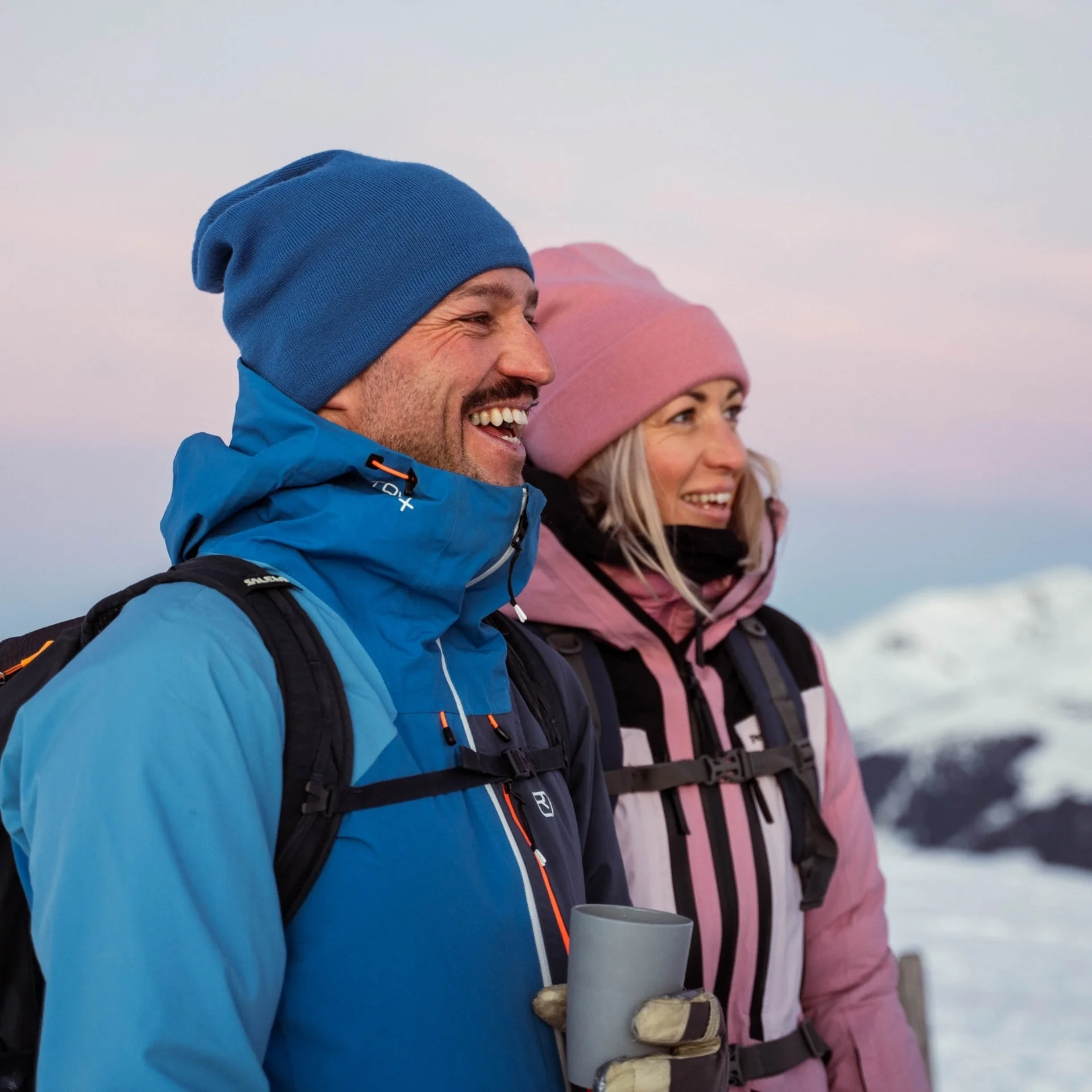 Wanderhotel Fröhliches Paar in Winterkleidung bei Sonnenuntergang in verschneiter Berglandschaft