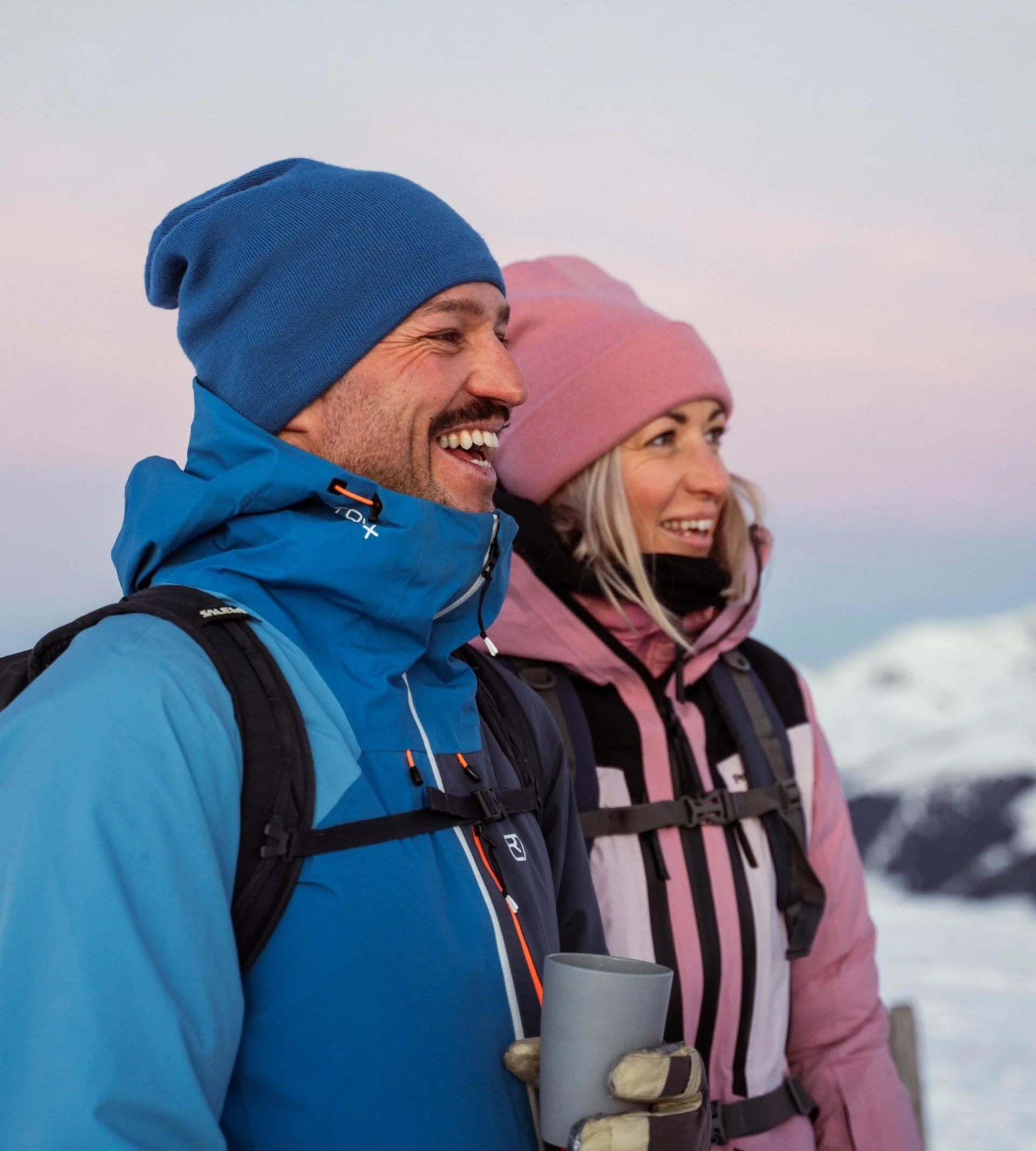 Wanderhotel Fröhliches Paar in Winterkleidung bei Sonnenuntergang in verschneiter Berglandschaft