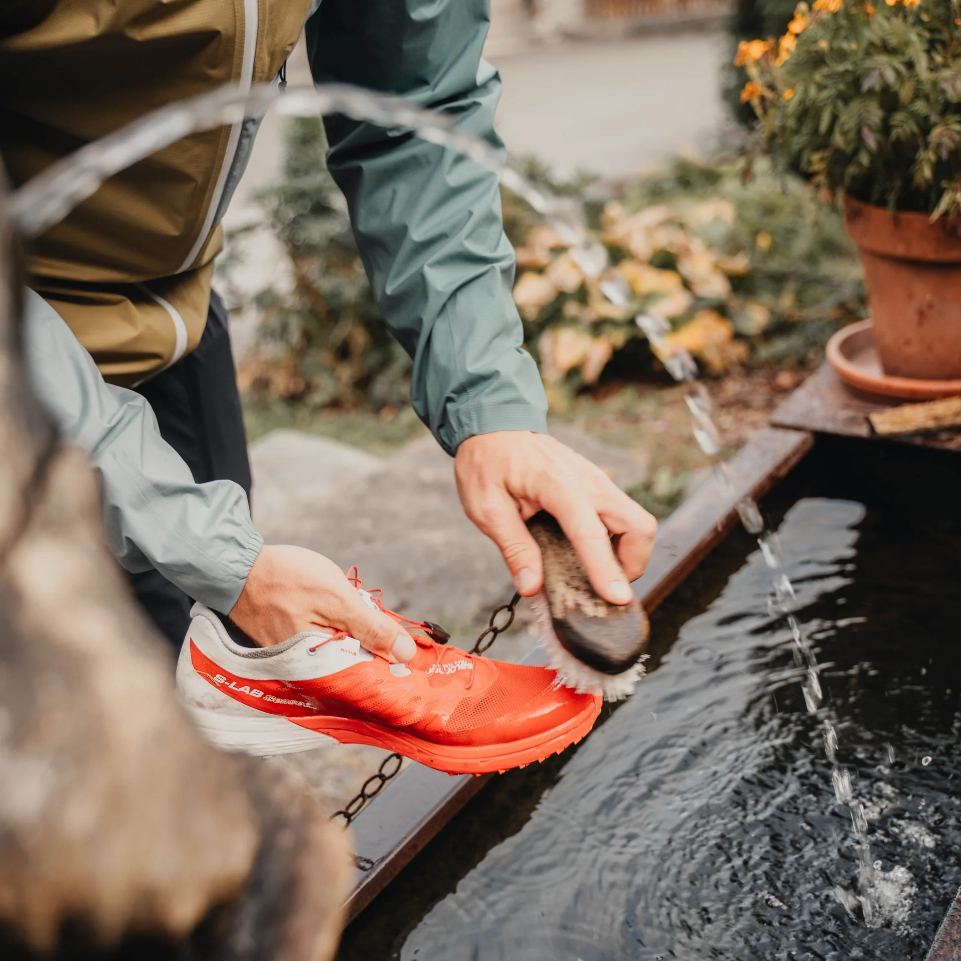 Person reinigt roten Sportschuh mit Bürste an Wasserquelle