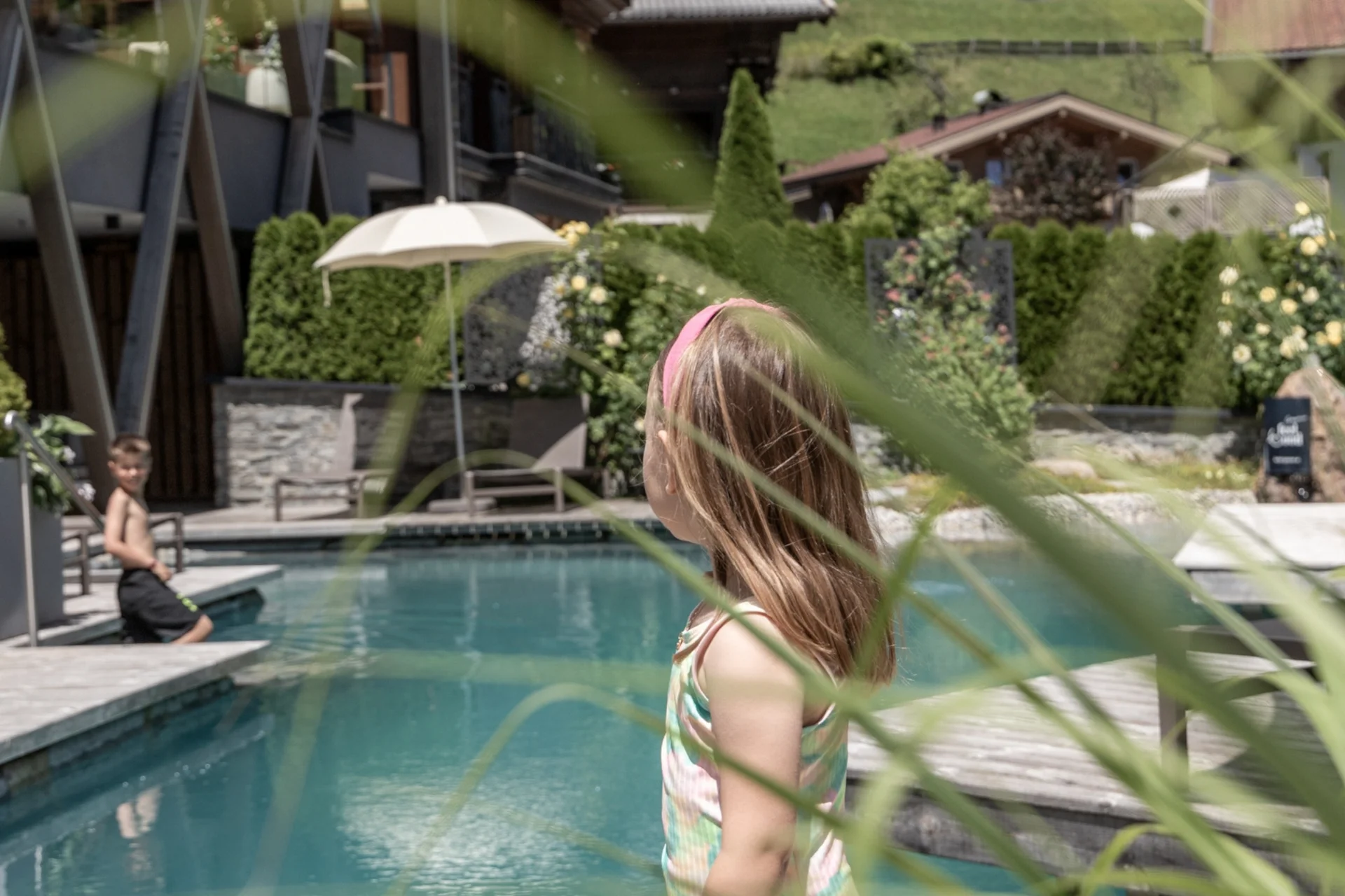 Spielend leichte Familienzeit im Hotel Gassner Kinder spielen an einem Außenpool in einem Garten mit Blick auf Hütten