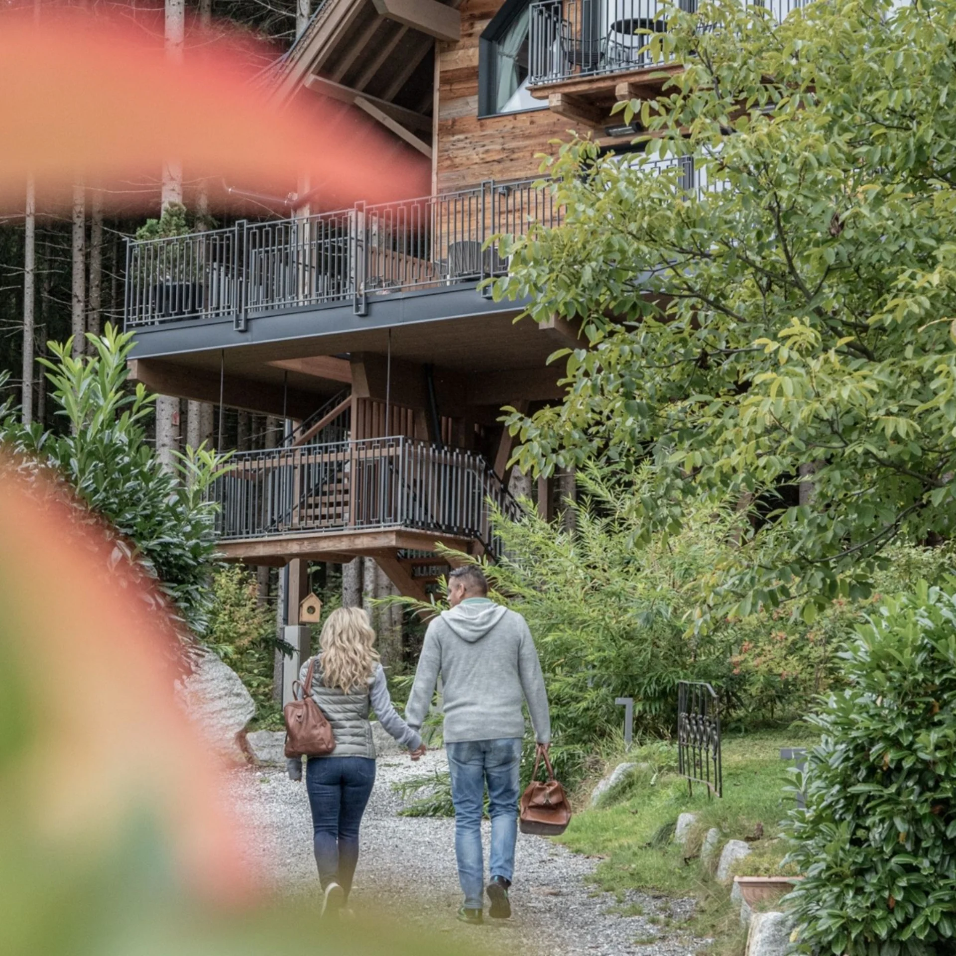Baumhaus Paar geht Hand in Hand auf einem Weg zu einem Holzhaus in grüner Umgebung