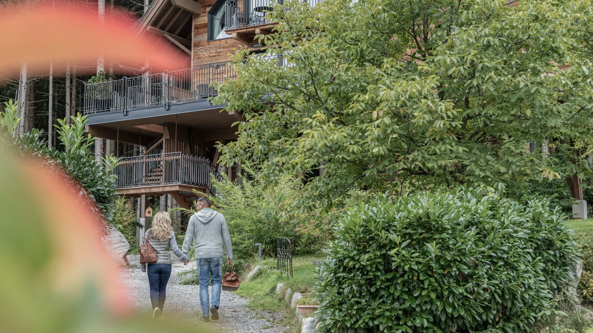 Home Paar geht Hand in Hand auf einem Weg zu einem Holzhaus in grüner Umgebung