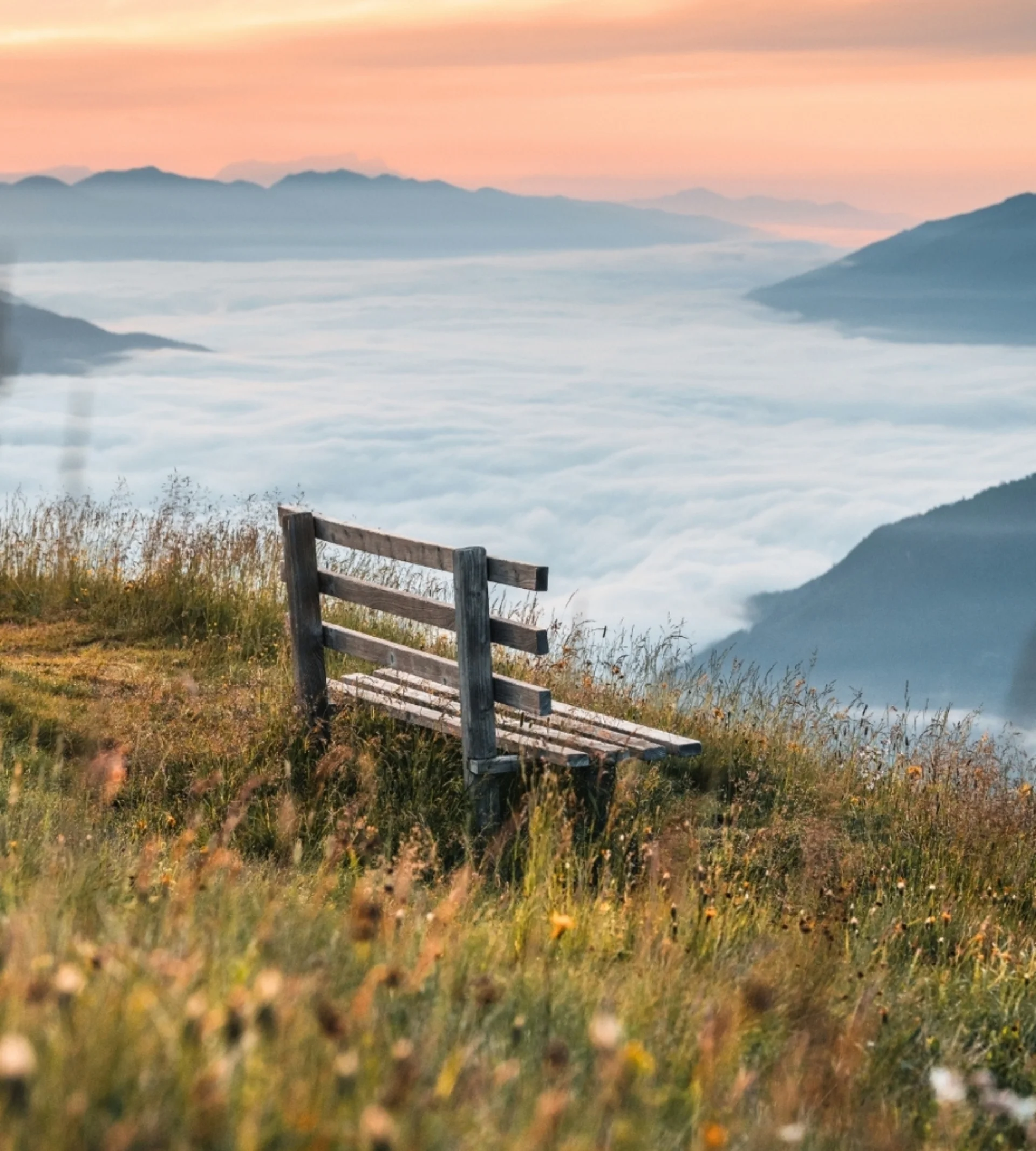 Wandern Holzbank auf Wiese mit Blick auf neblige Berge bei Sonnenuntergang