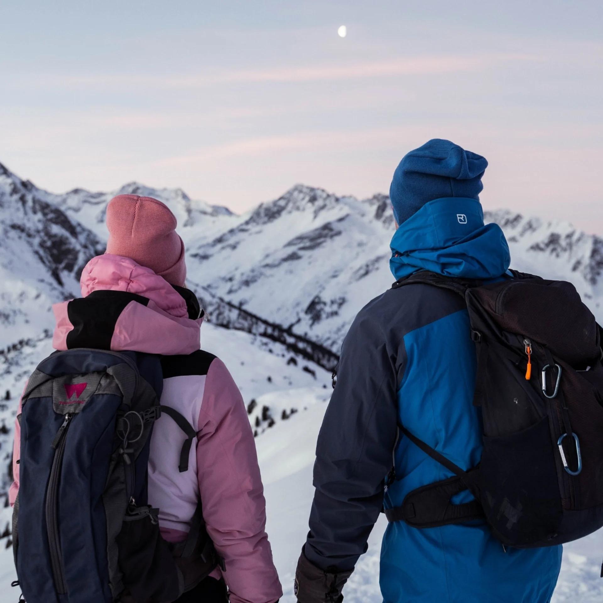 Jobs Zwei Wanderer in Winterkleidung blicken auf verschneite Berge bei Dämmerung