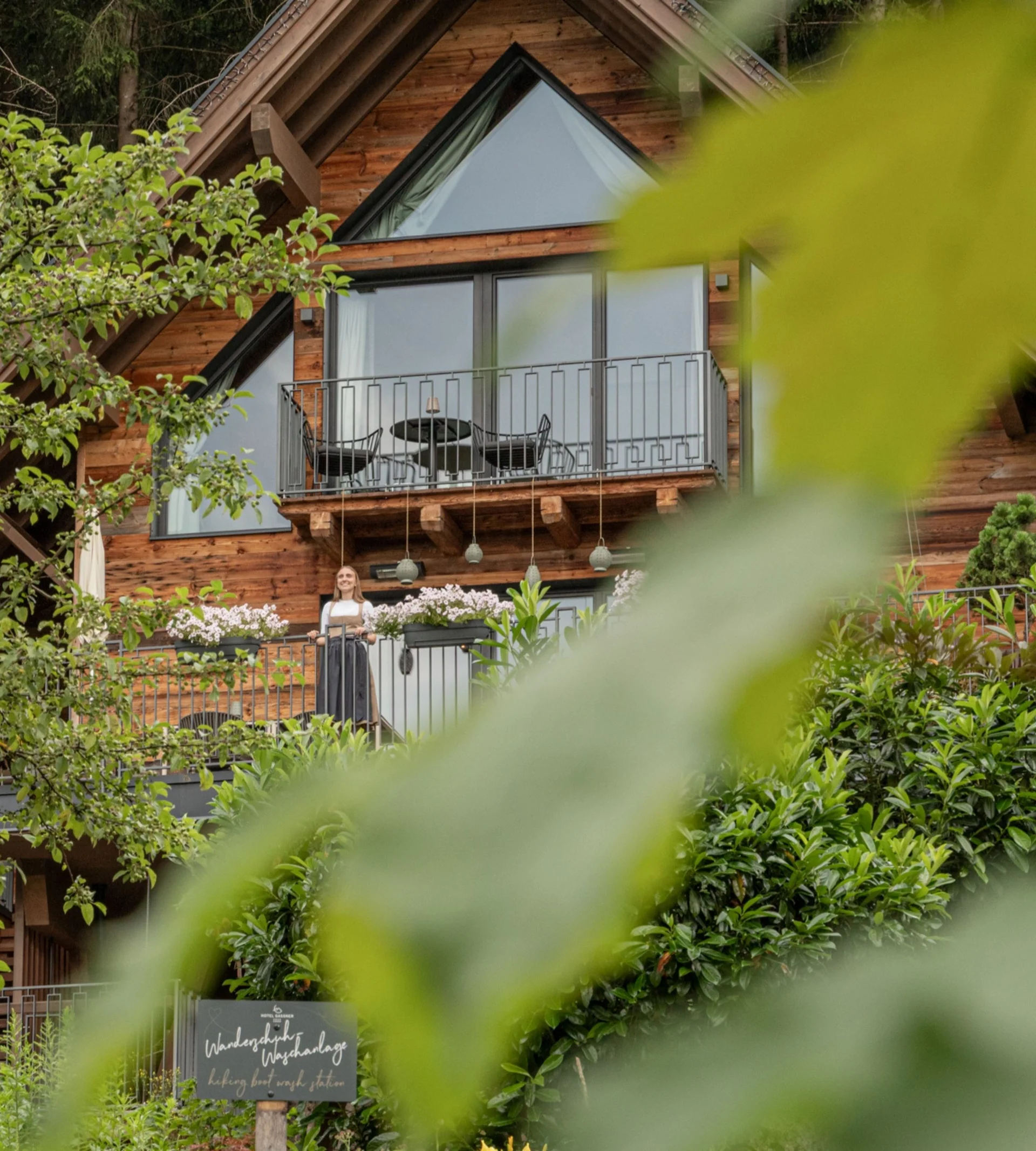 Spielend leichte Familienzeit im Hotel Gassner Holzhaus mit Balkon und einer Person, umgeben von grünem Laub