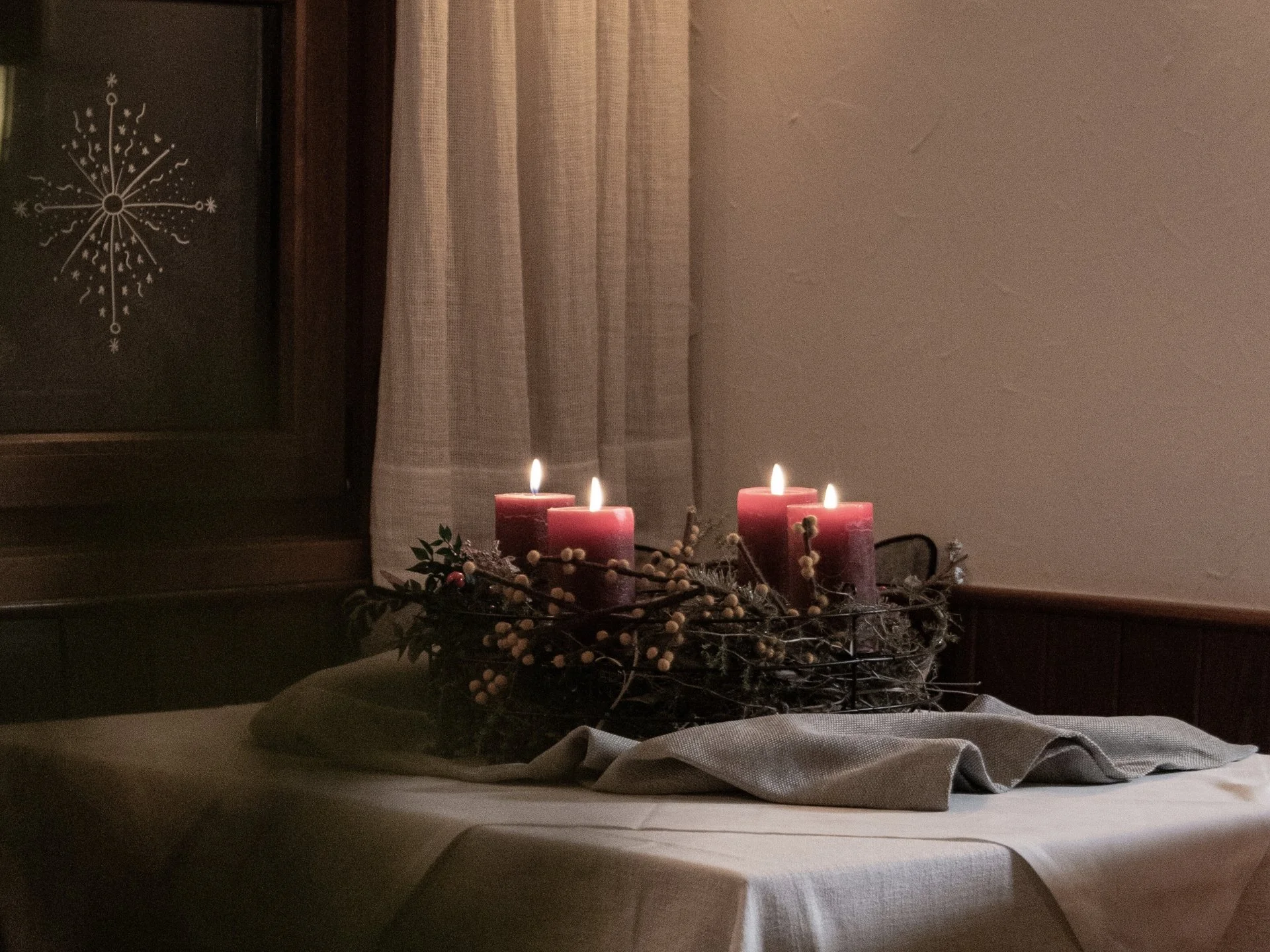 Vier brennende rote Kerzen auf einem mit Tuch bedeckten Tisch am Fenster