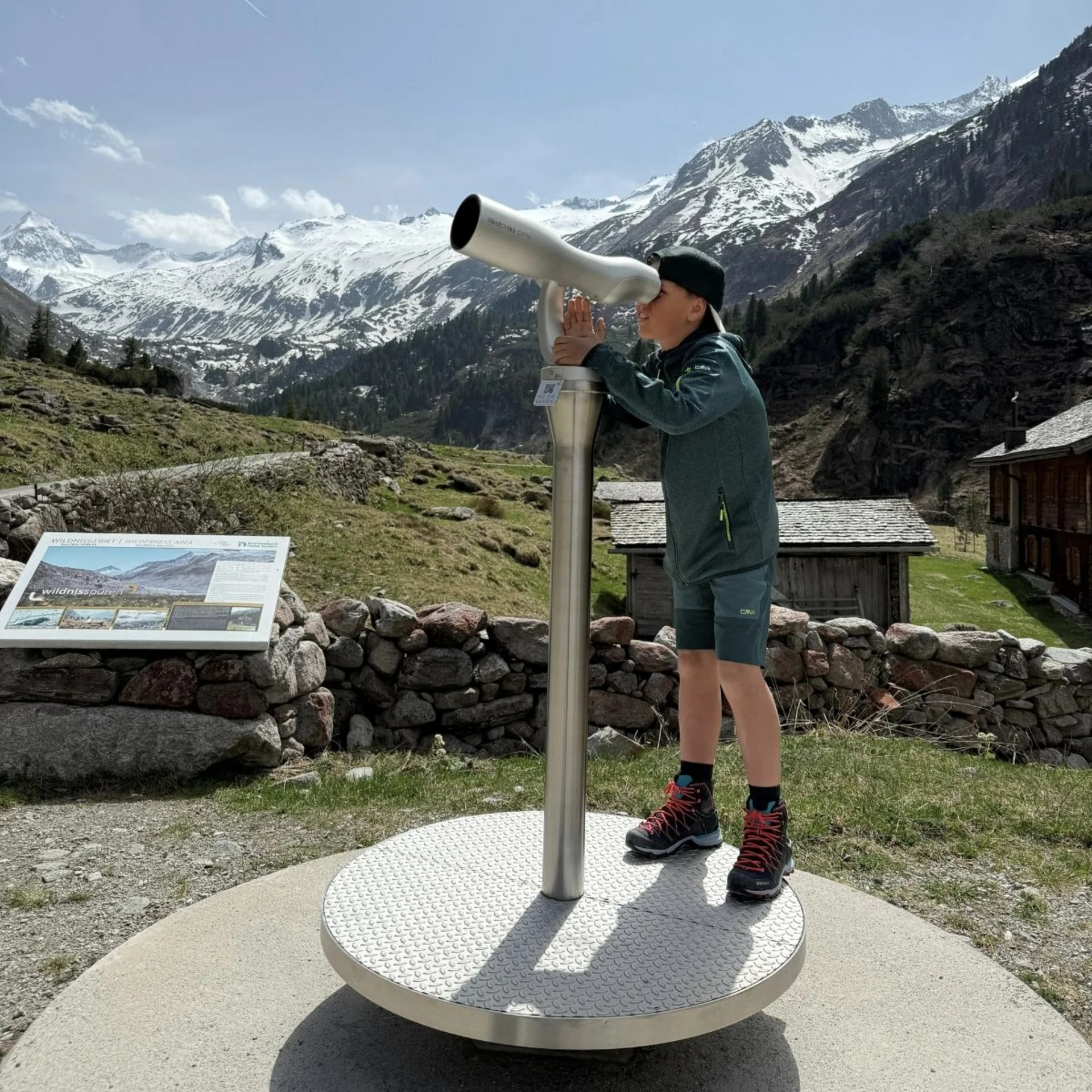 Spielend leichte Familienzeit im Hotel Gassner Kind schaut durch großes Fernglas vor schneebedeckten Bergen im Tal