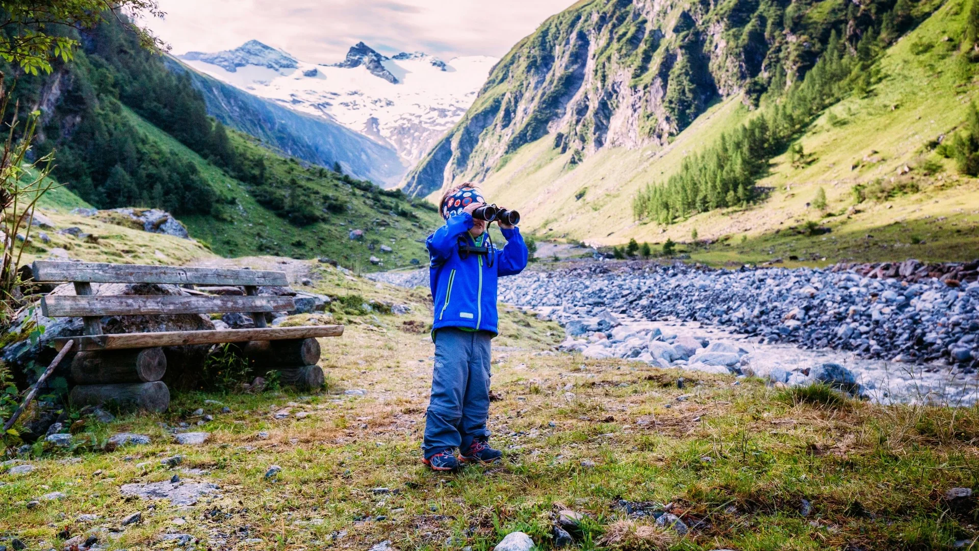 Family time Child with binoculars in front of an alpine valley with glacier and stream