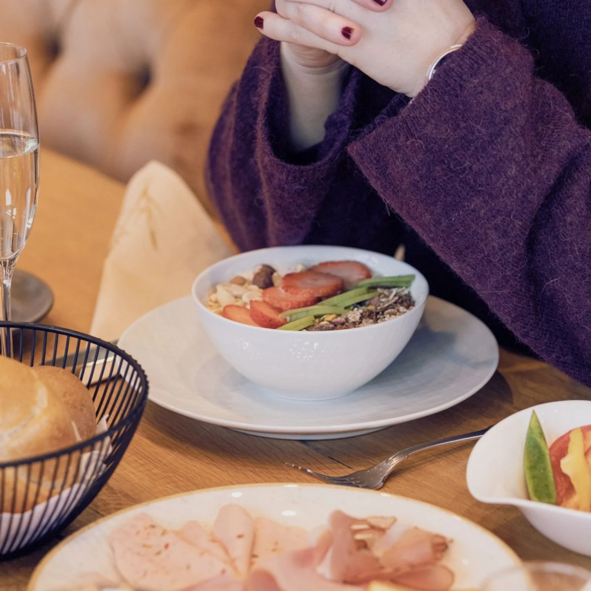 Babymoon im Gassner Baumhaus Person mit lila Pullover isst Müsli mit Früchten am Frühstückstisch