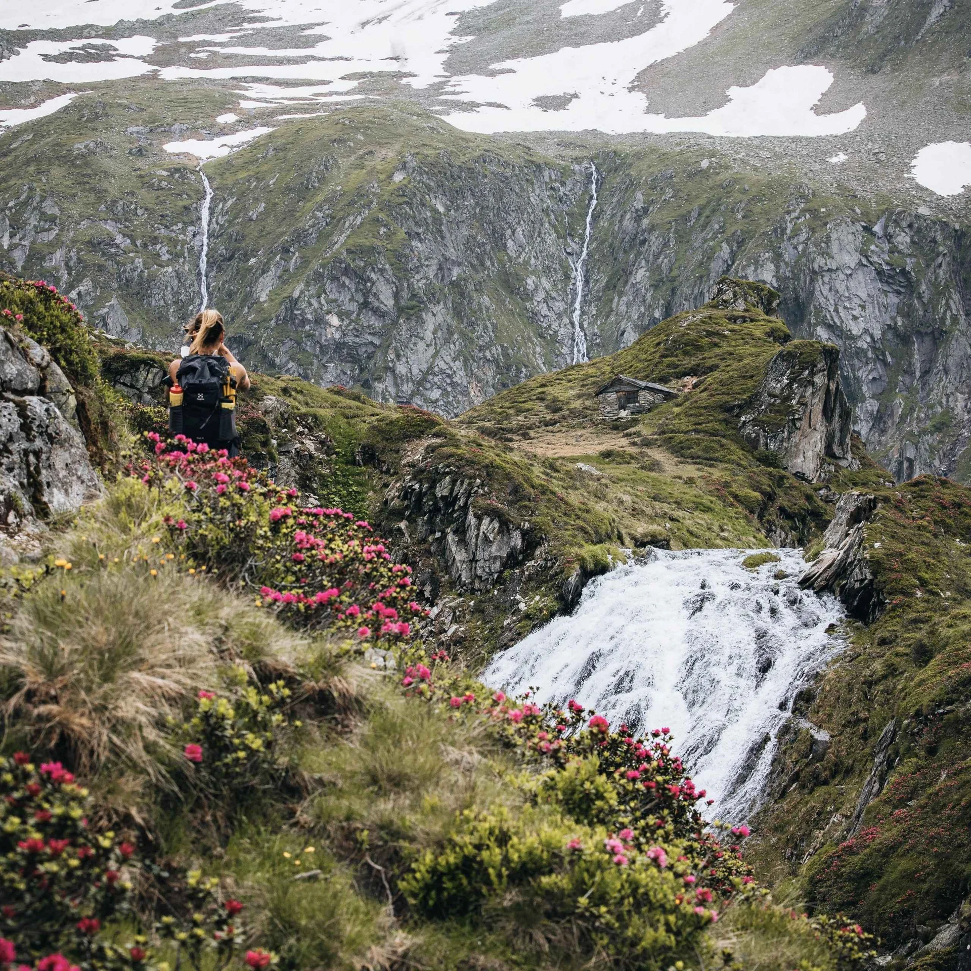 Wanderer blickt auf Wasserfälle und schneebedeckte Berge in Alpenlandschaft