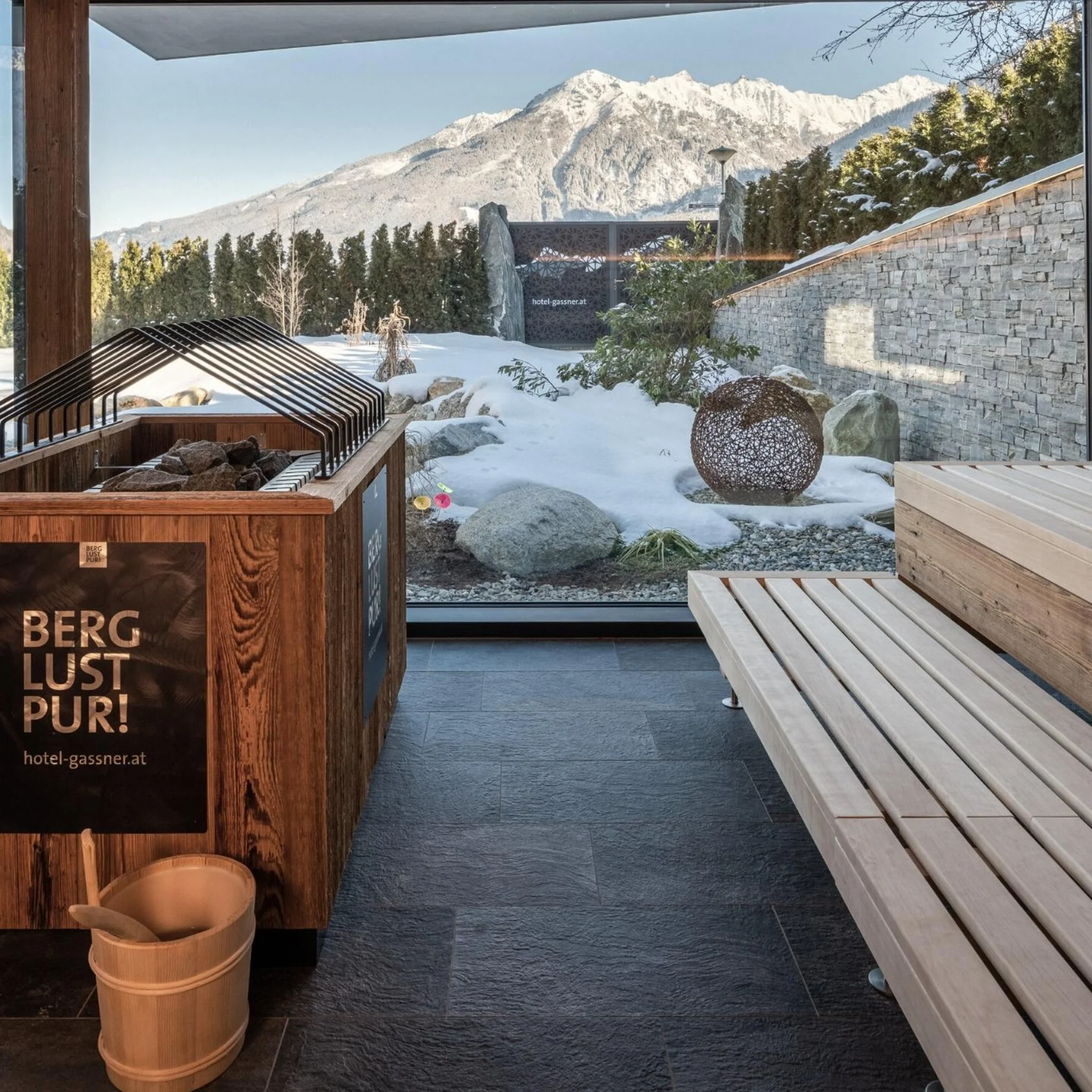 Sauna with panoramic window showing snow-covered mountains and garden