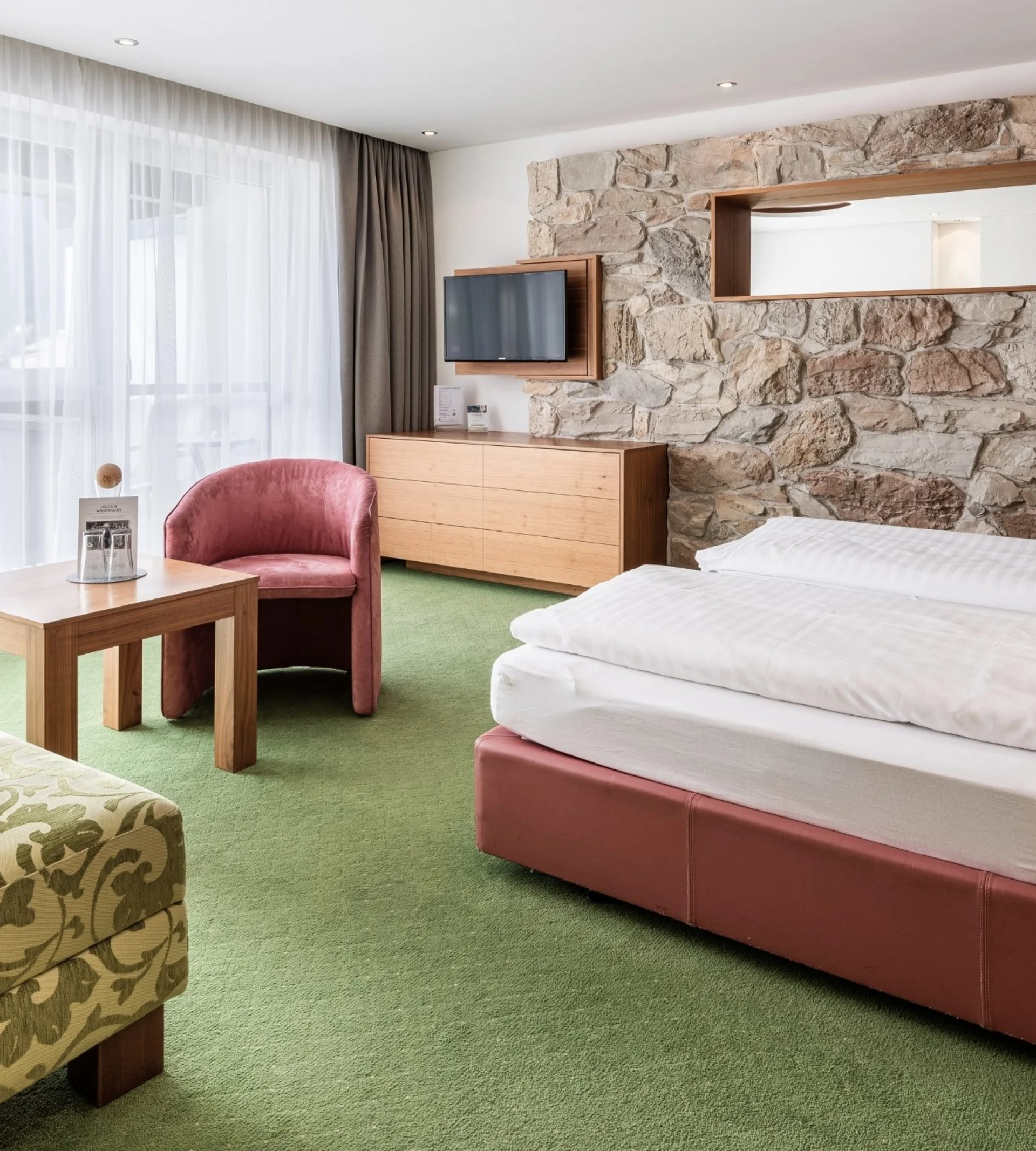 Spielend leichte Familienzeit im Hotel Gassner Gemütliches Hotelzimmer mit Doppelbett, Steinwand und Sitzbereich