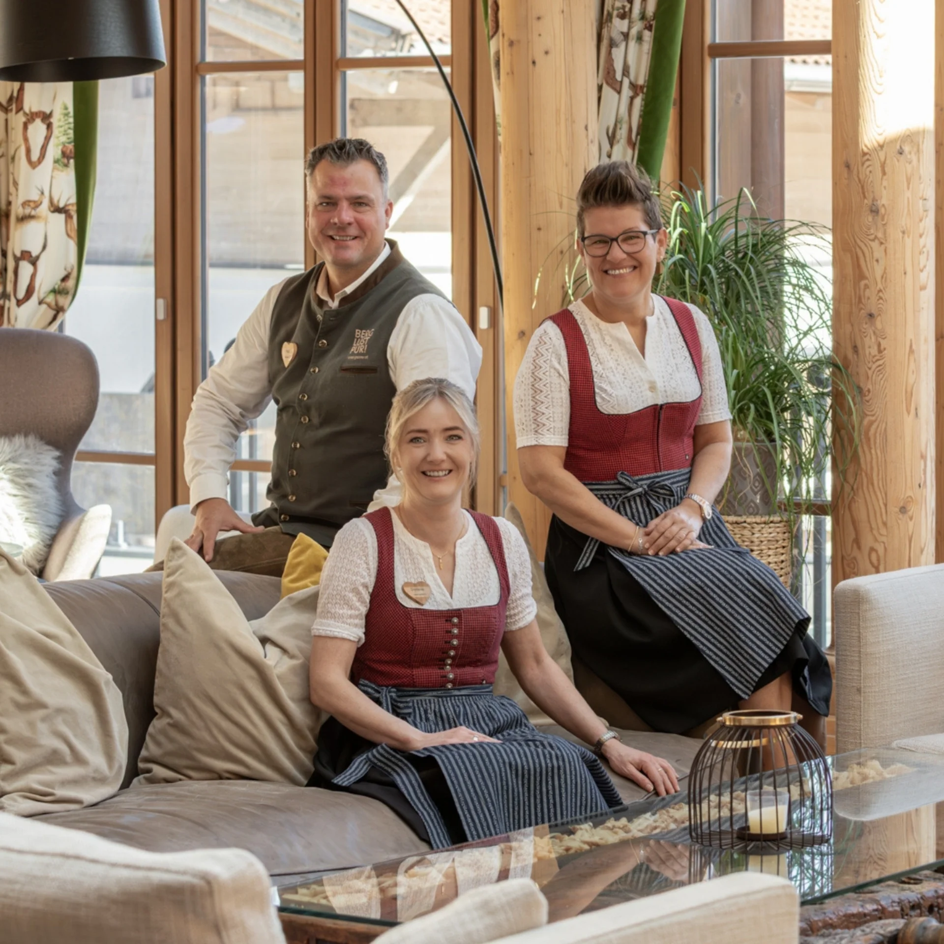 Vier Personen in Trachten sitzen am Holzsteg neben einem Naturteich