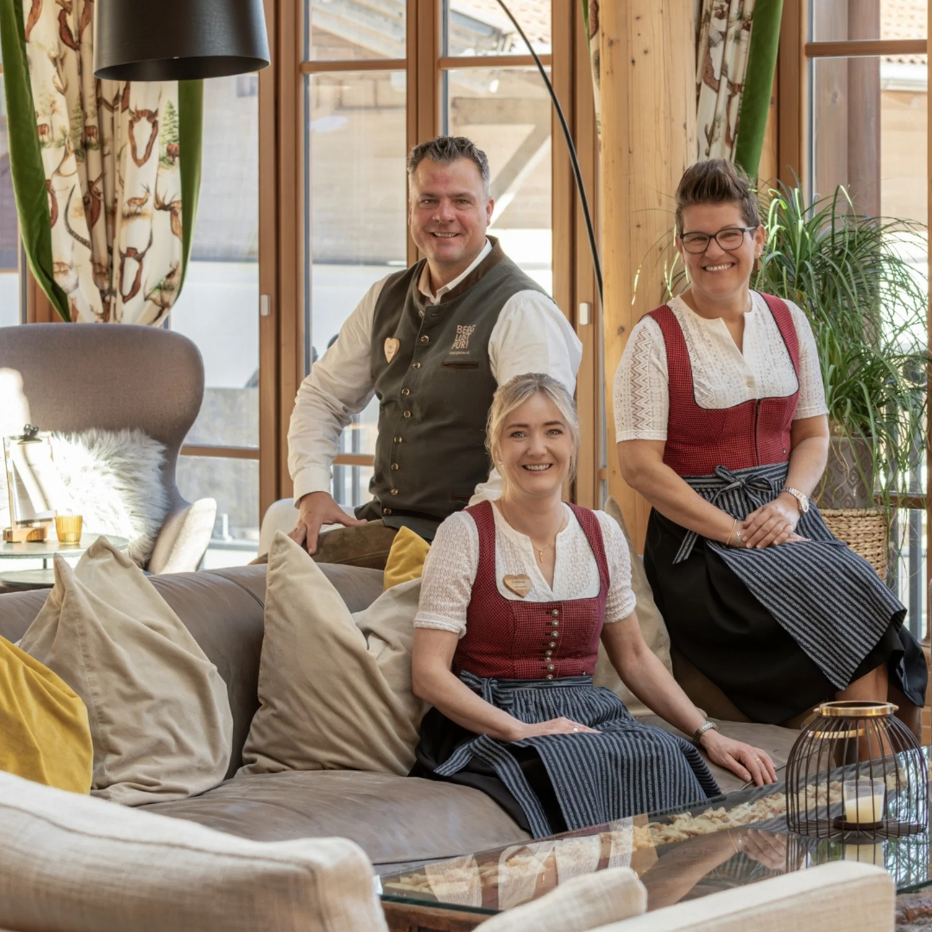 Four people in traditional attire sitting on a wooden deck by a natural pond