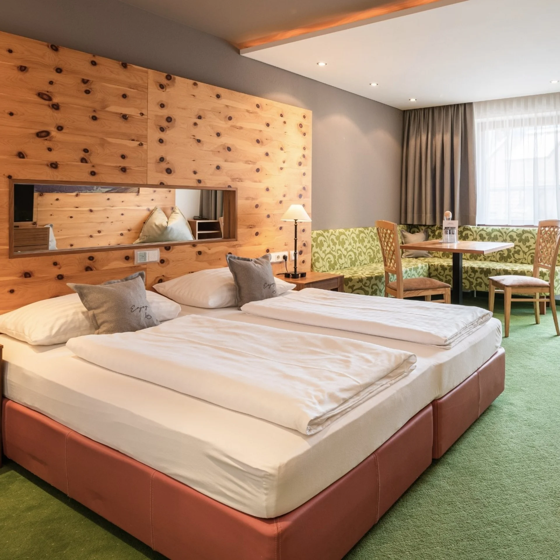 Bright hotel room with double bed, wooden wall, seating area and green carpet