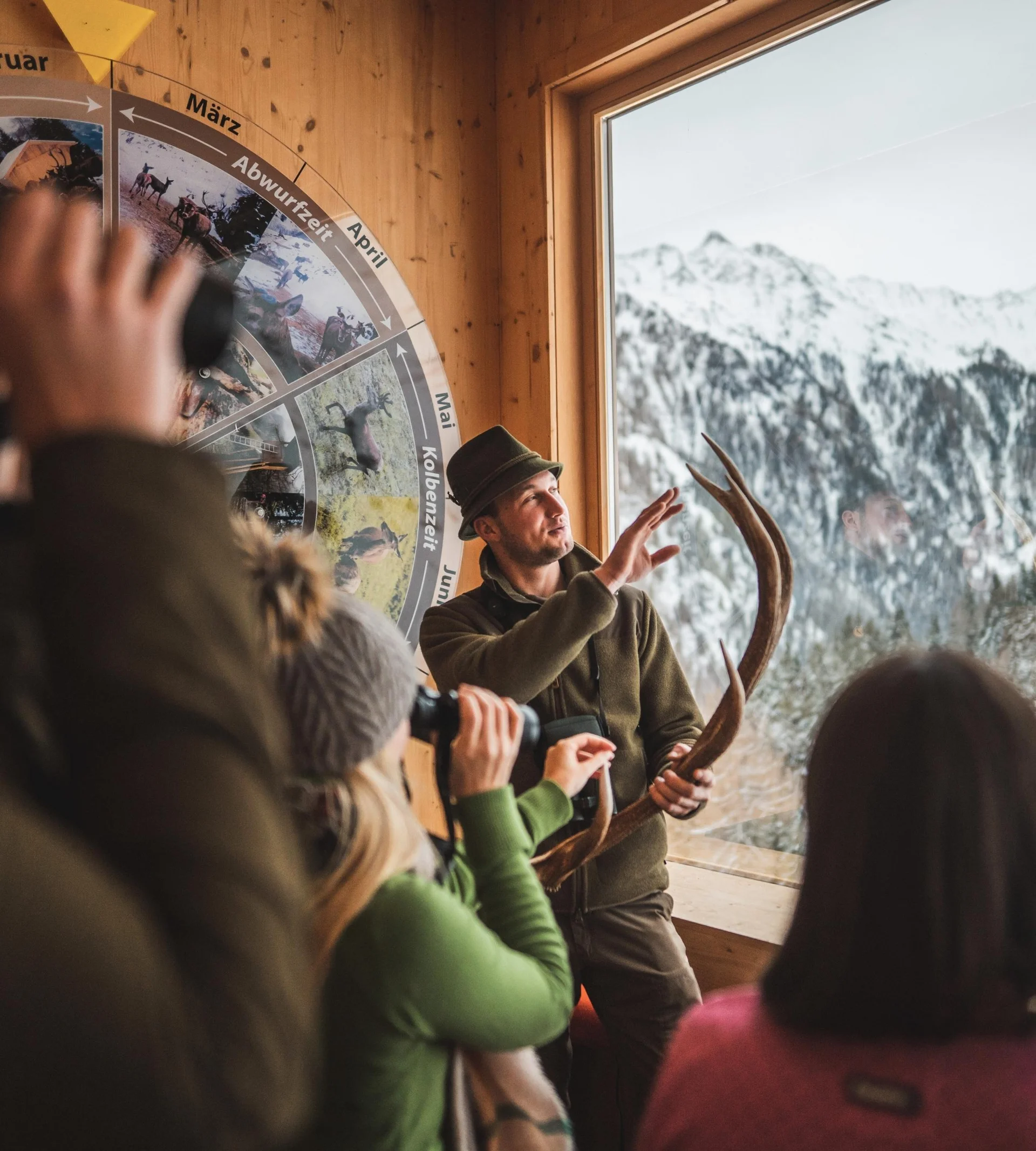 Hiking Service Hunter explains antlers and wildlife calendar to visitors in mountain cabin