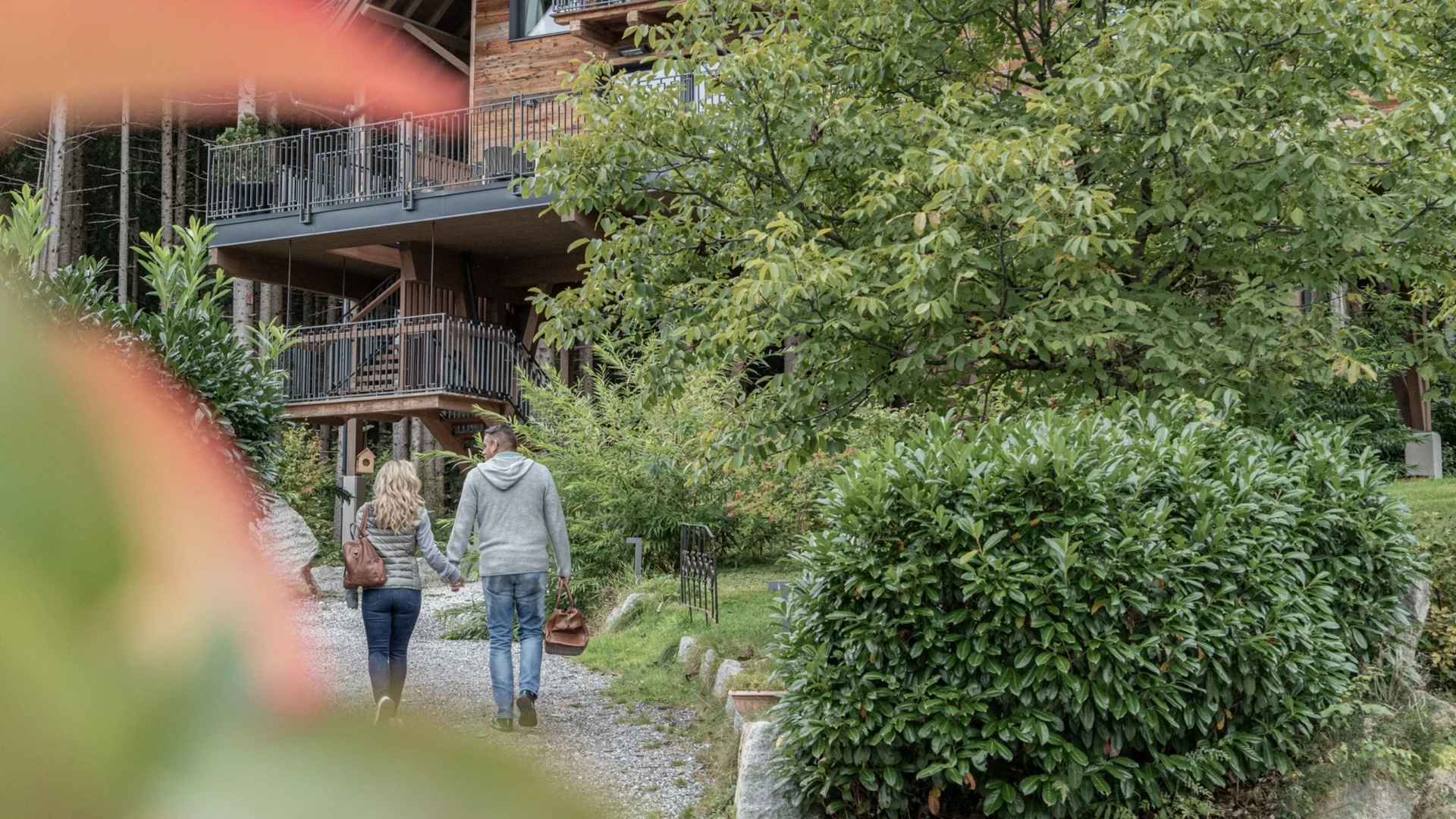 Home Paar hält Händchen und geht auf einem Kiesweg neben grünen Büschen und einem Haus