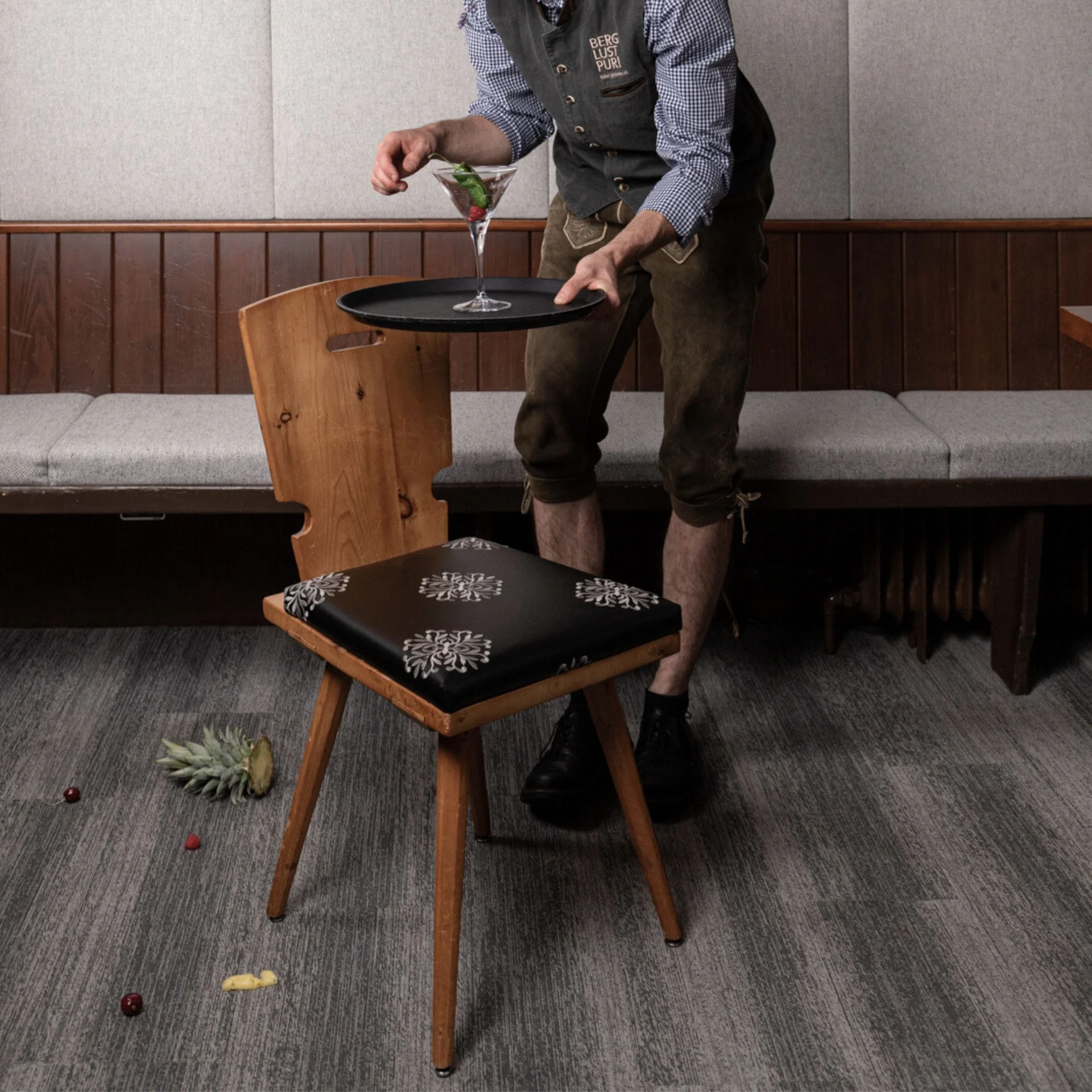 Kellner in Tracht serviert Getränk auf Serviertablett an Holzstuhl in Restaurant