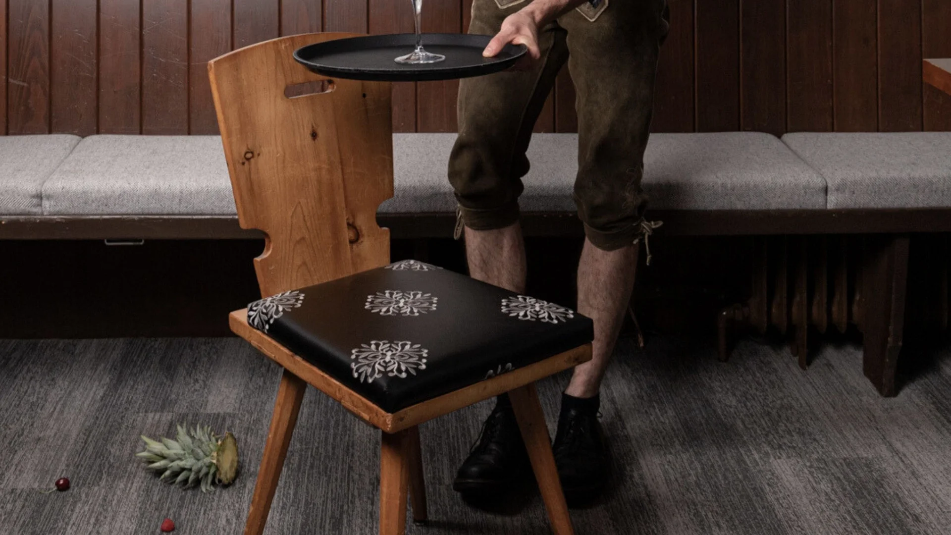Lehrlingsausbildung Kellner in Tracht serviert Getränk auf Serviertablett an Holzstuhl in Restaurant