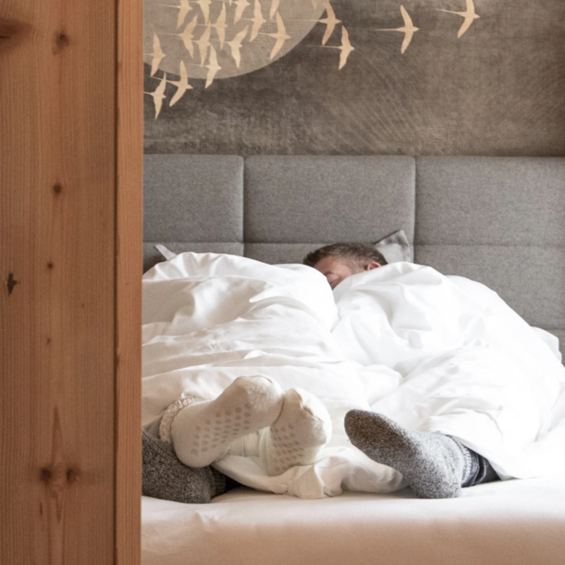 Two people lying in bed with socks under white covers in a wooden room
