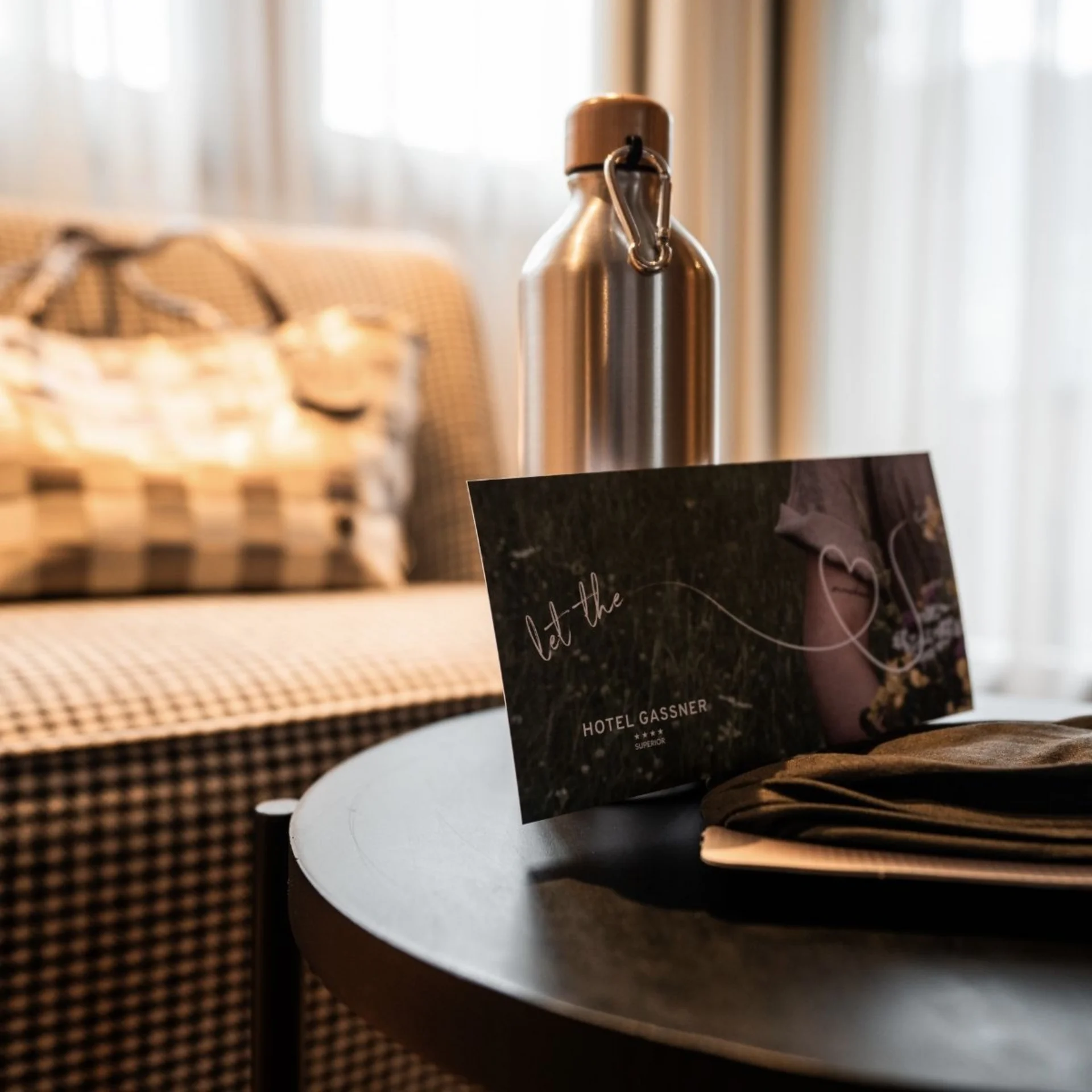 Familien.Zeit Metallflasche und Hotel Gassner Karte auf schwarzem Tisch vor kariertem Sofa