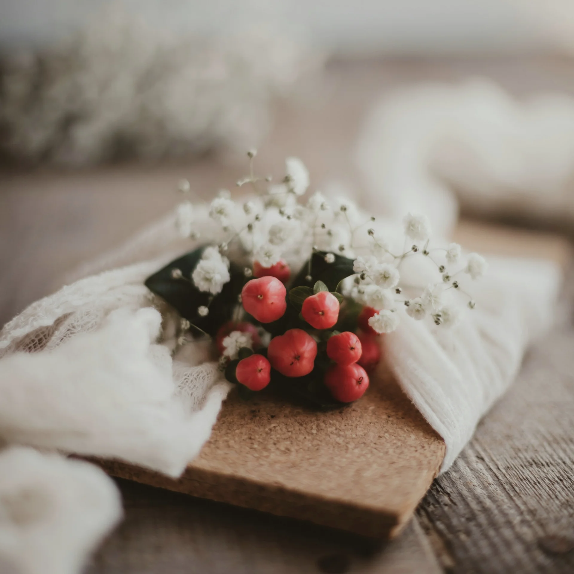 Rote Beeren und weiße Blüten auf einem Holzbrett mit weißem Stoff