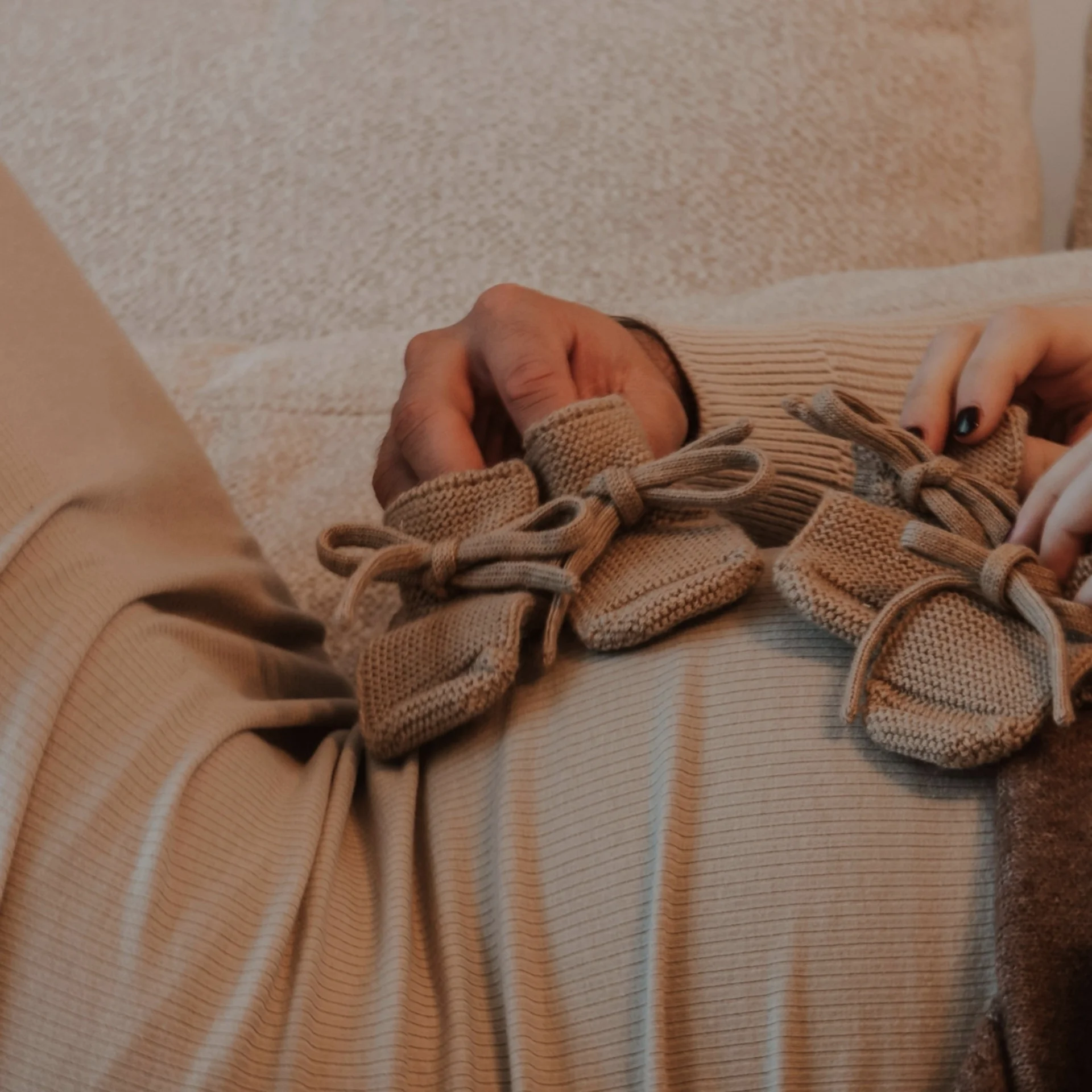 Babymoon im Gassner Baumhaus Zwei Personen halten kleine gestrickte Babyschuhe auf einem Bauch