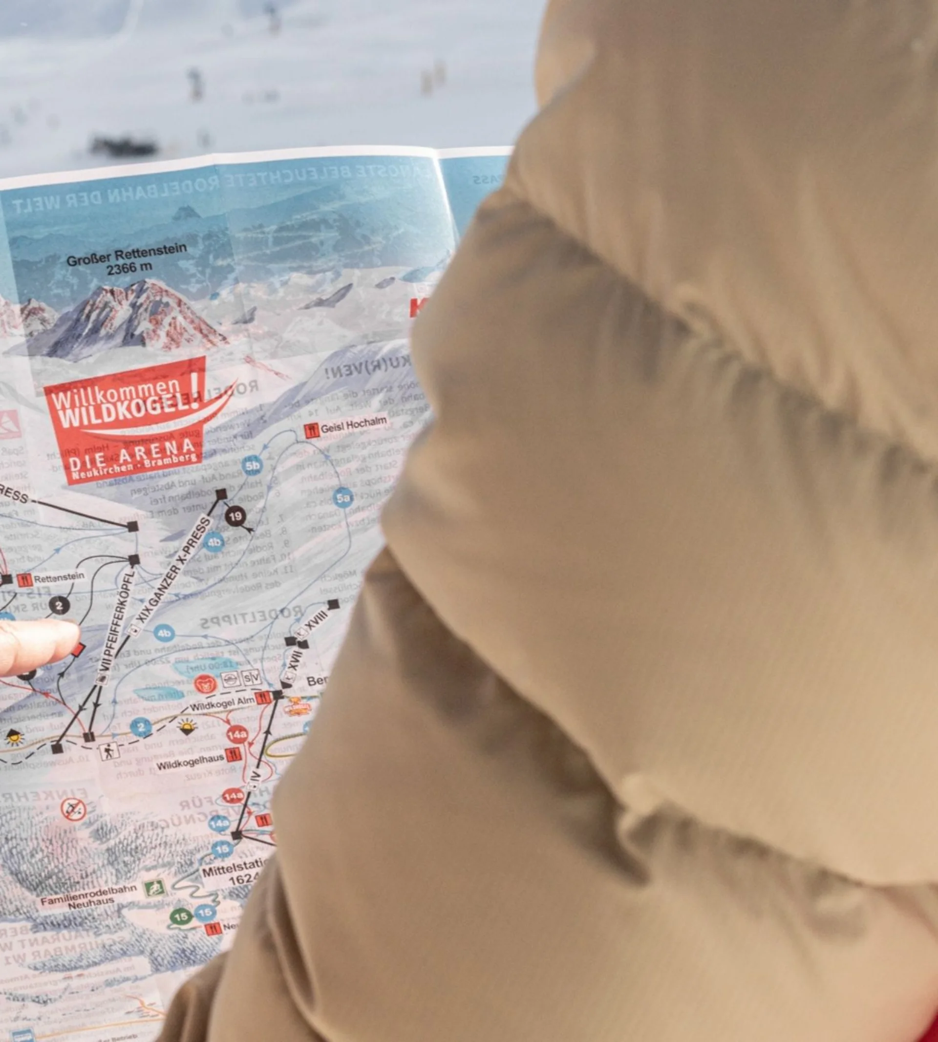 Person zeigt auf einen Skipistenplan in einer verschneiten Berglandschaft