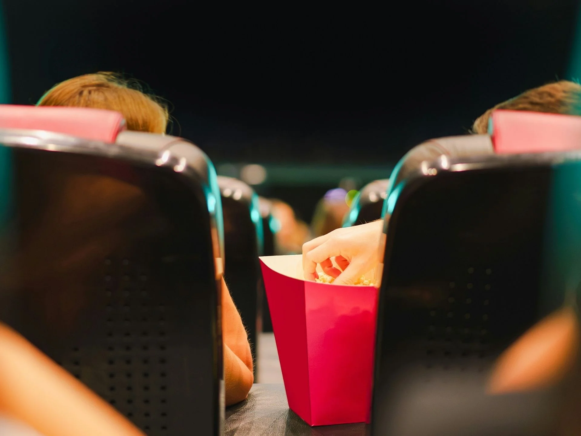 Menschen sitzen im Kinosaal, eine Person greift in die Popcornschachtel