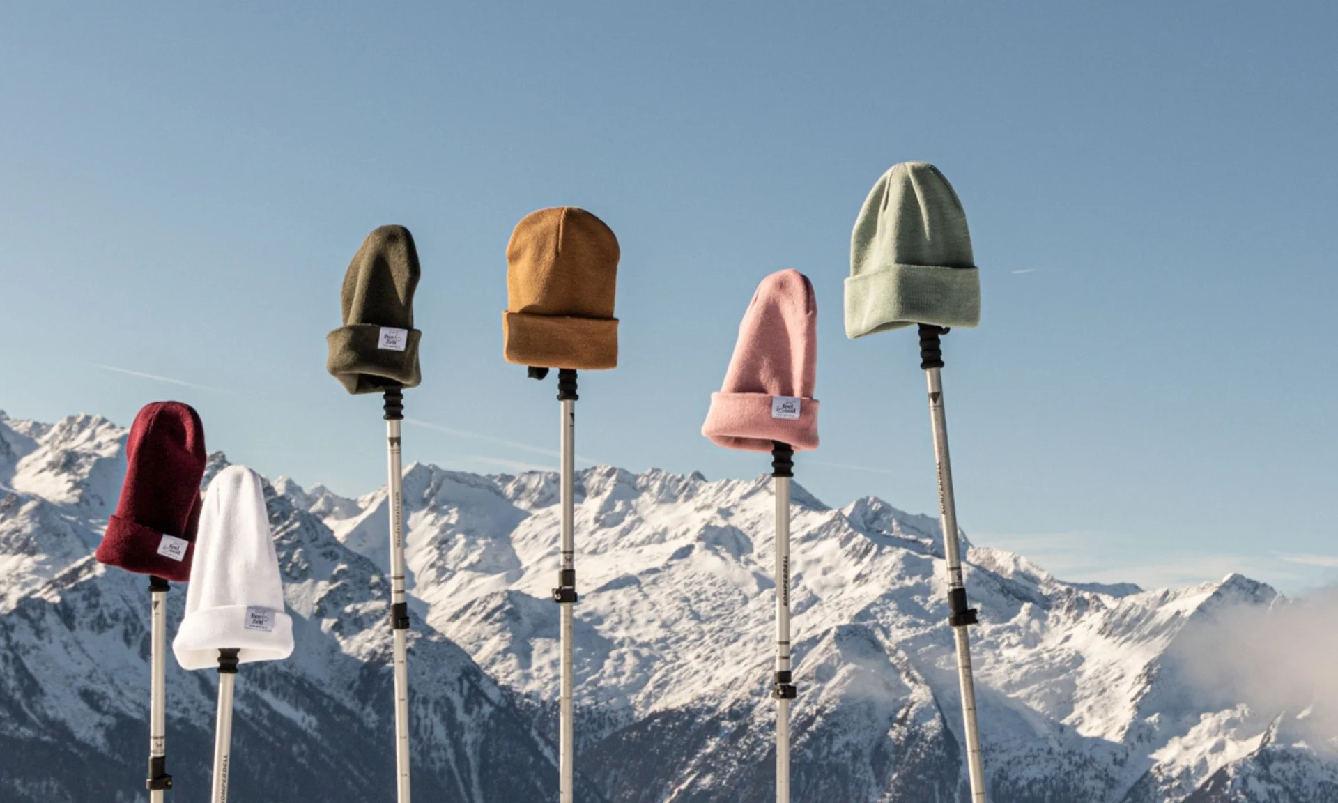 Wintermützen auf Stöcken vor schneebedeckten Bergen und blauem Himmel
