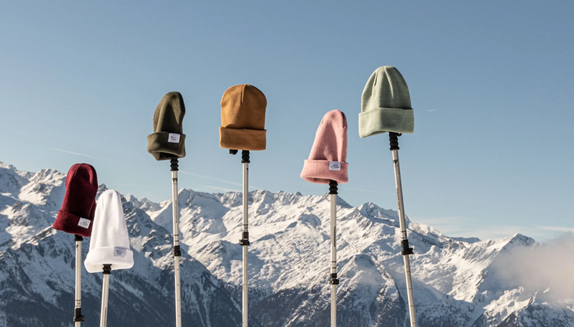 Wintermützen auf Stöcken vor schneebedeckten Bergen und blauem Himmel