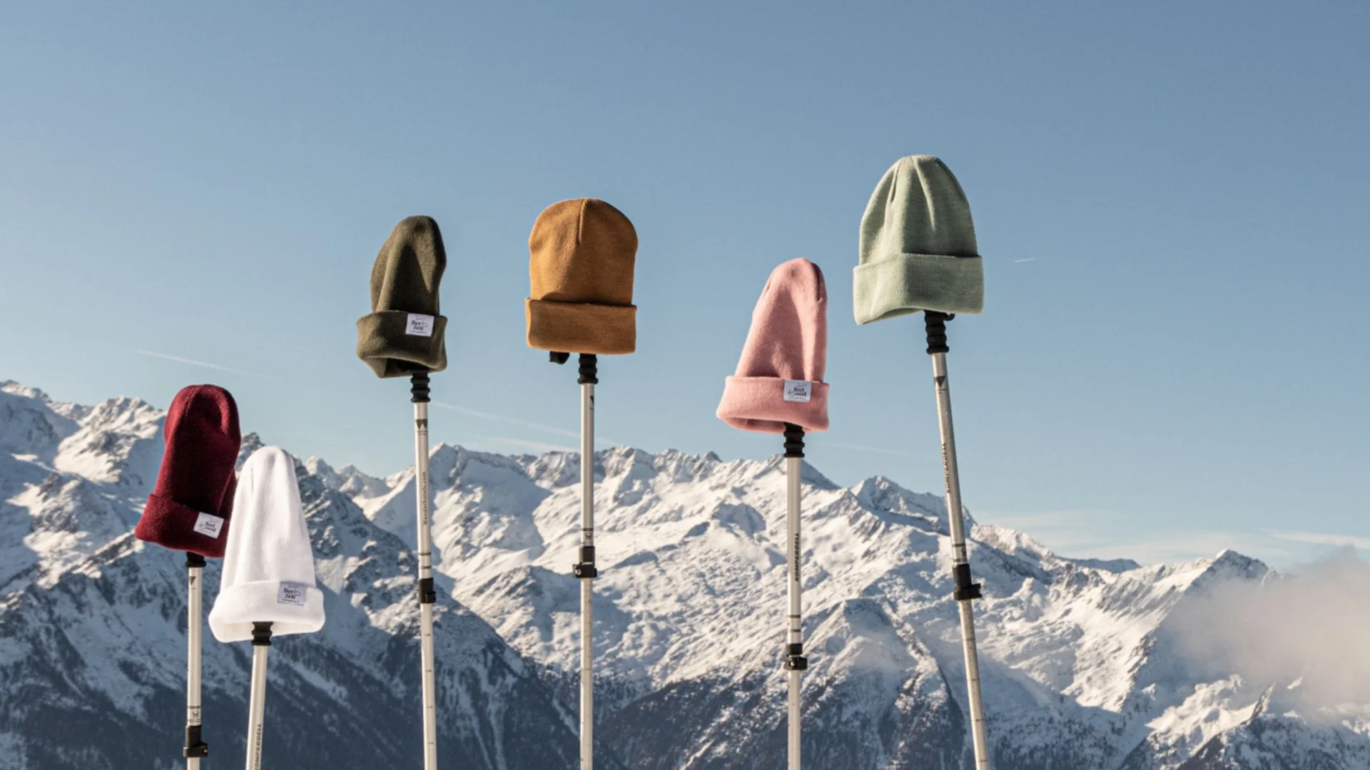 Wintermützen auf Stöcken vor schneebedeckten Bergen und blauem Himmel