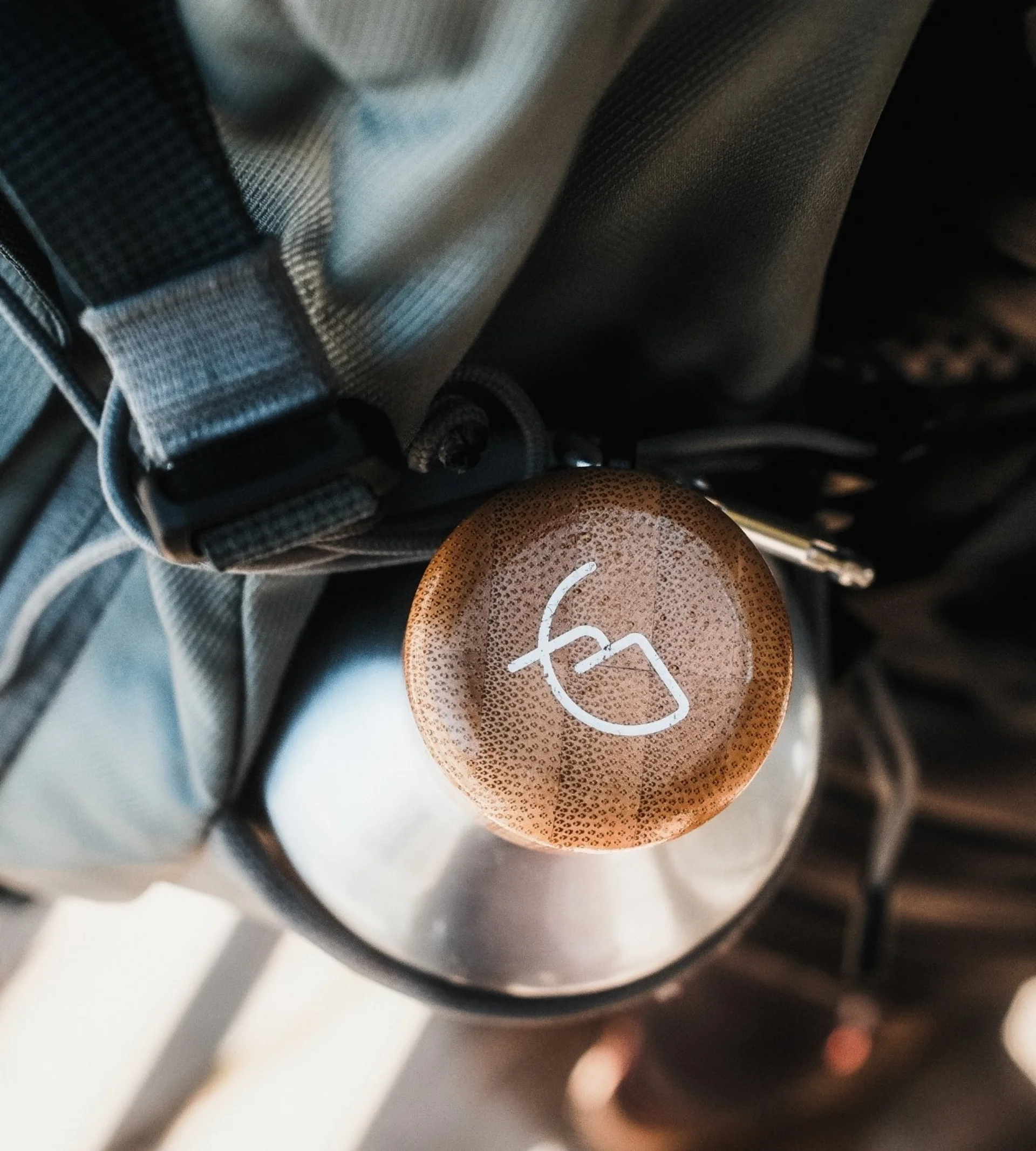 Home Brauner Anhänger an grauem Rucksack mit Metallflasche im Hintergrund