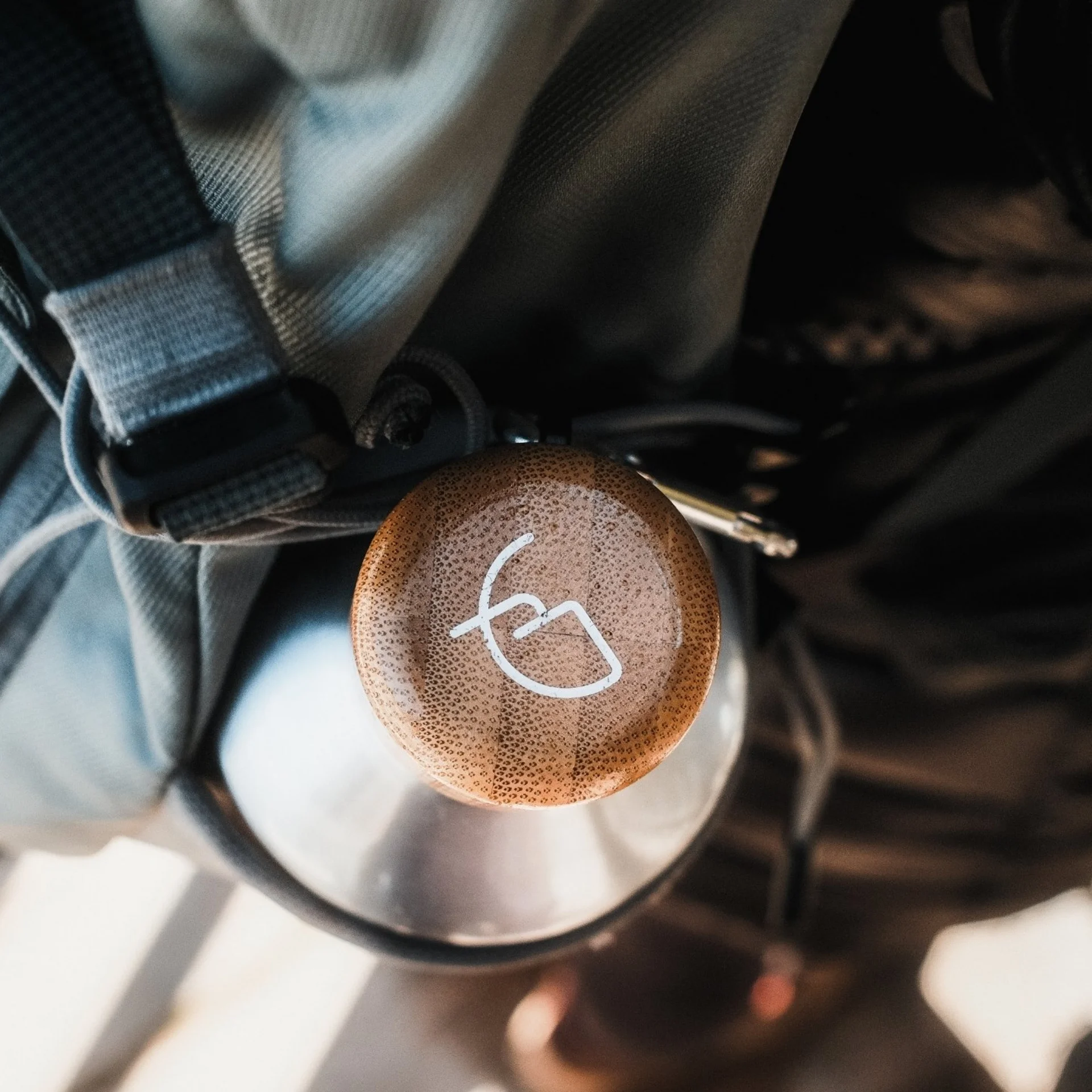 Brown pendant hanging on gray backpack with metal bottle in background