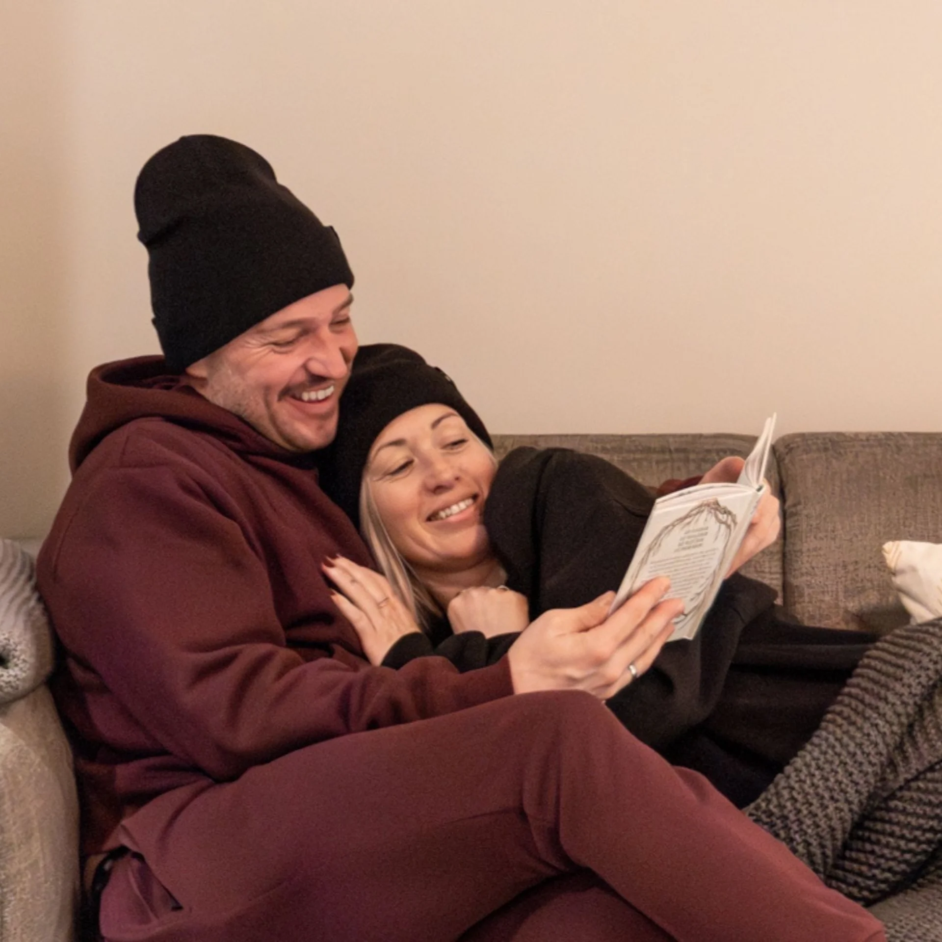 First.Date – Baumhaus Paar in warmer Kleidung liest zusammen auf dem Sofa unter einer Decke