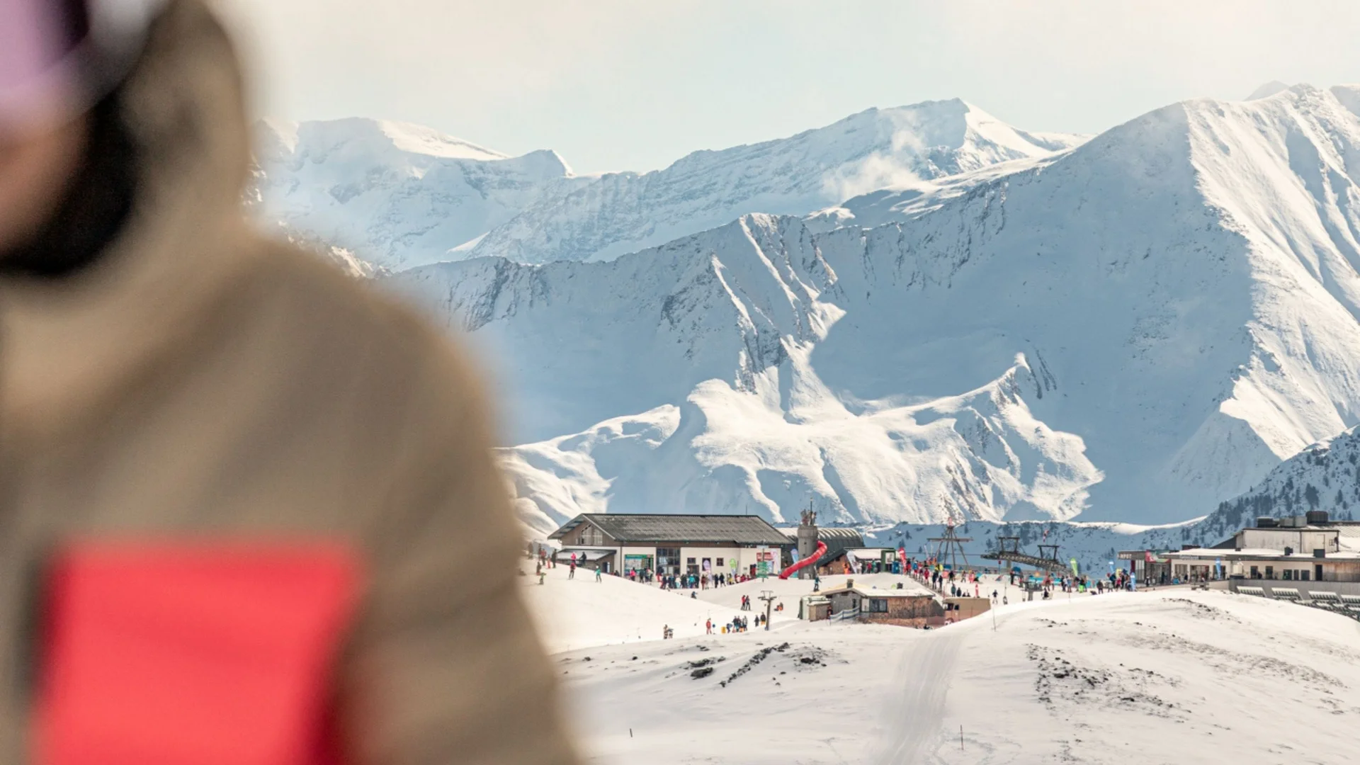Schneebedeckte Berghütte mit Menschen vor großen Bergen im Hintergrund