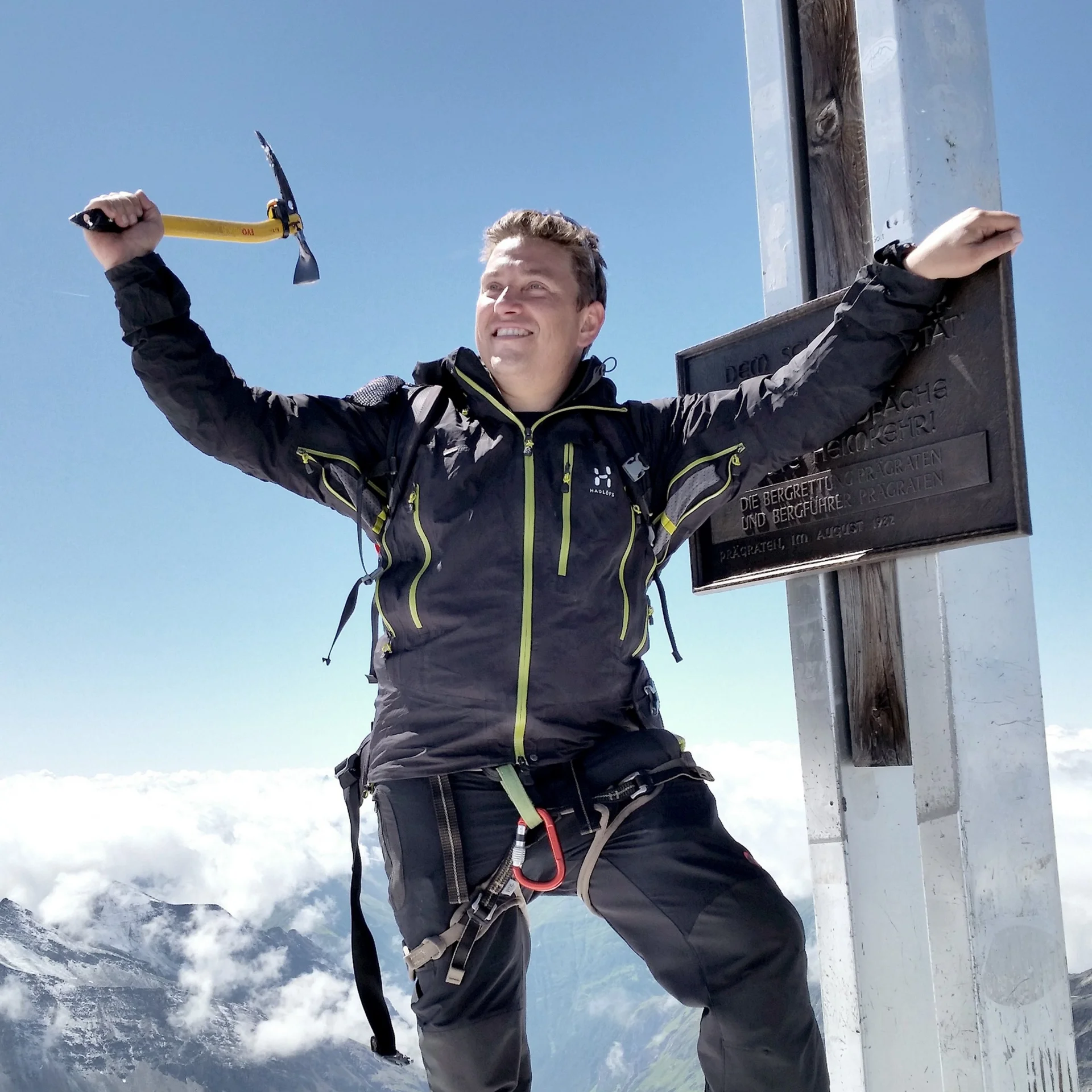 Mann mit Eispickel auf Berggipfel vor Bergpanorama und Wolken