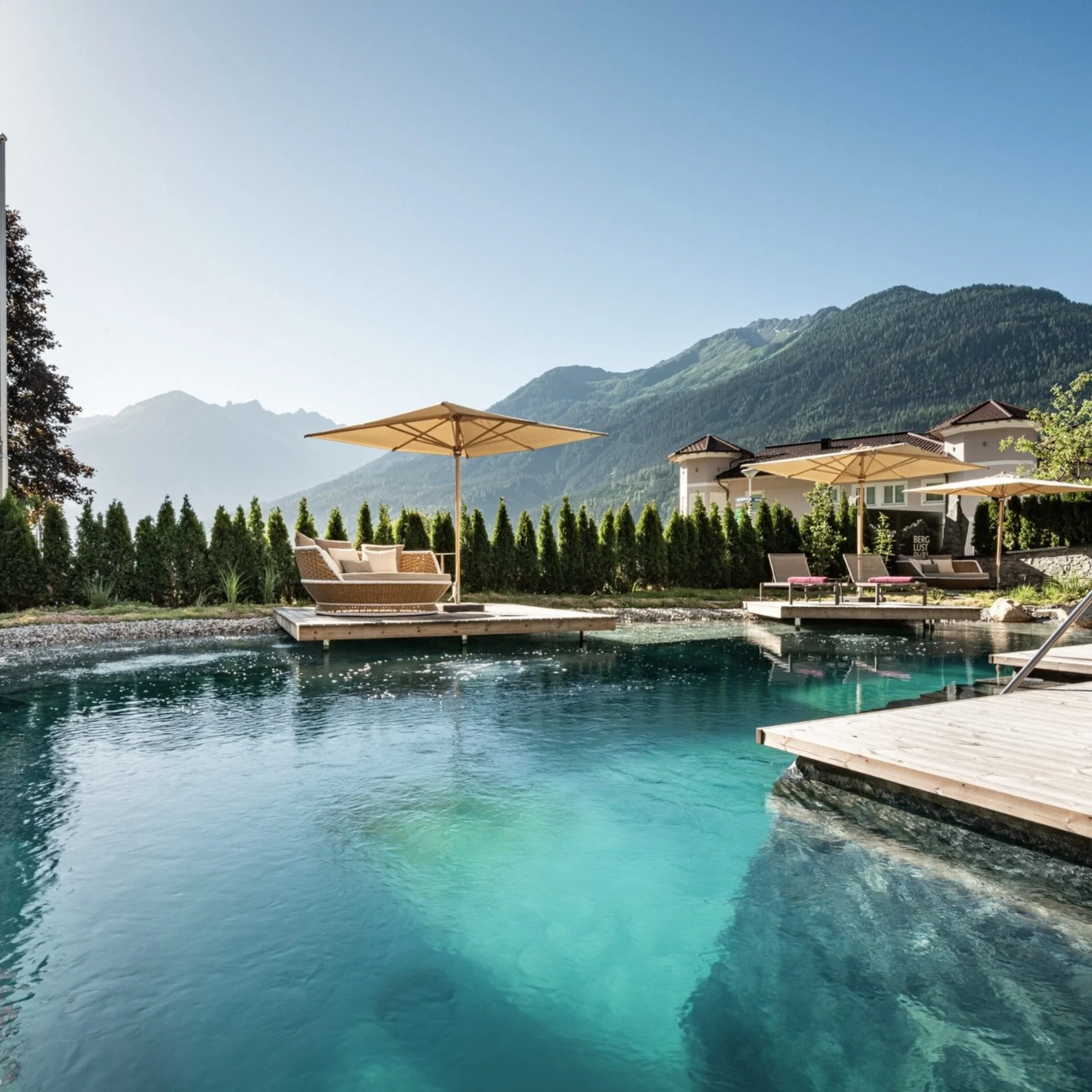 Außenpool mit Liegestühlen und Sonnenschirmen vor Bergkulisse